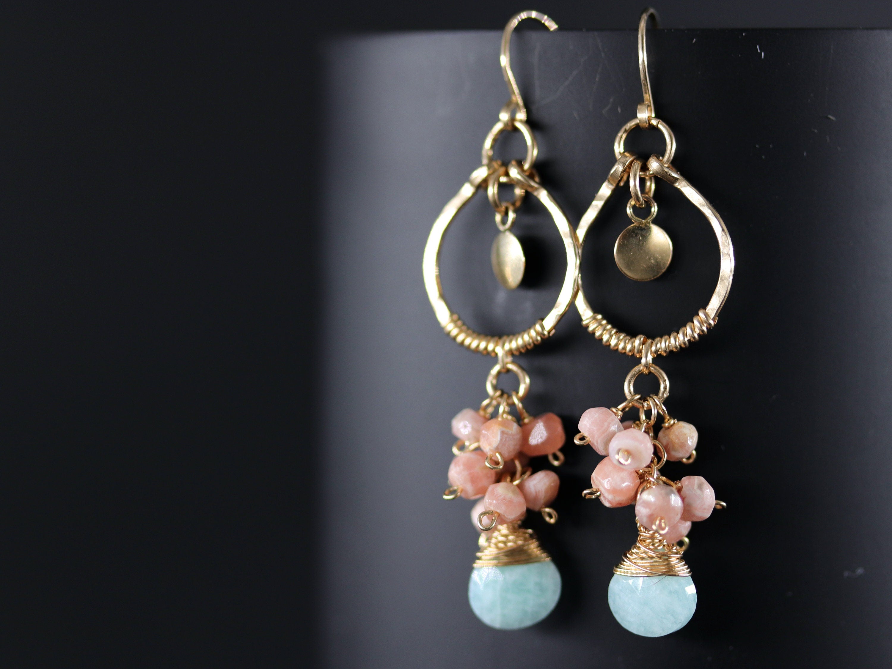 May include: Gold hoop earrings with a dangling cluster of light pink and light blue stones.