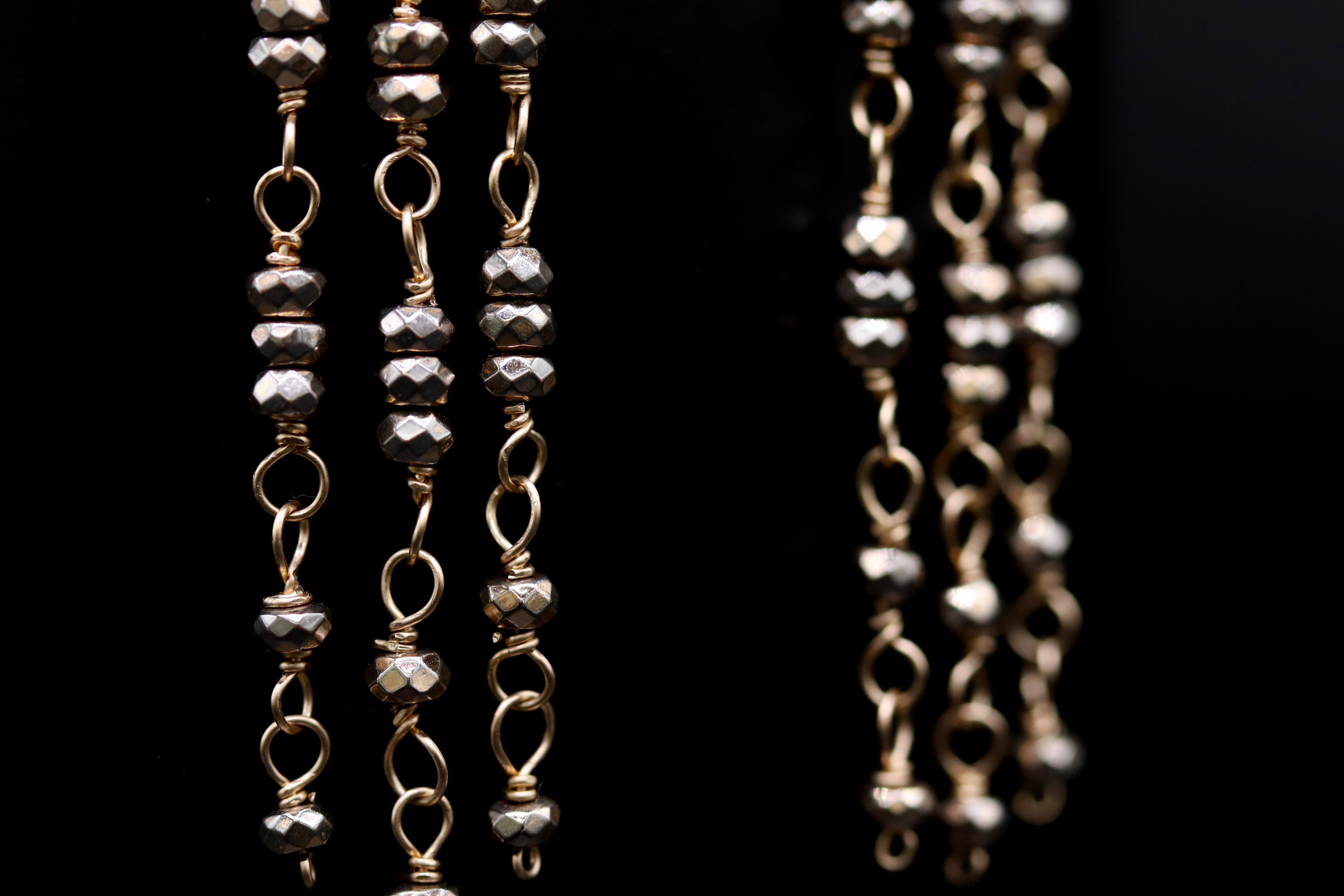 A close-up view of a chain with multiple rows of small, shiny, metallic beads or stones attached to it.