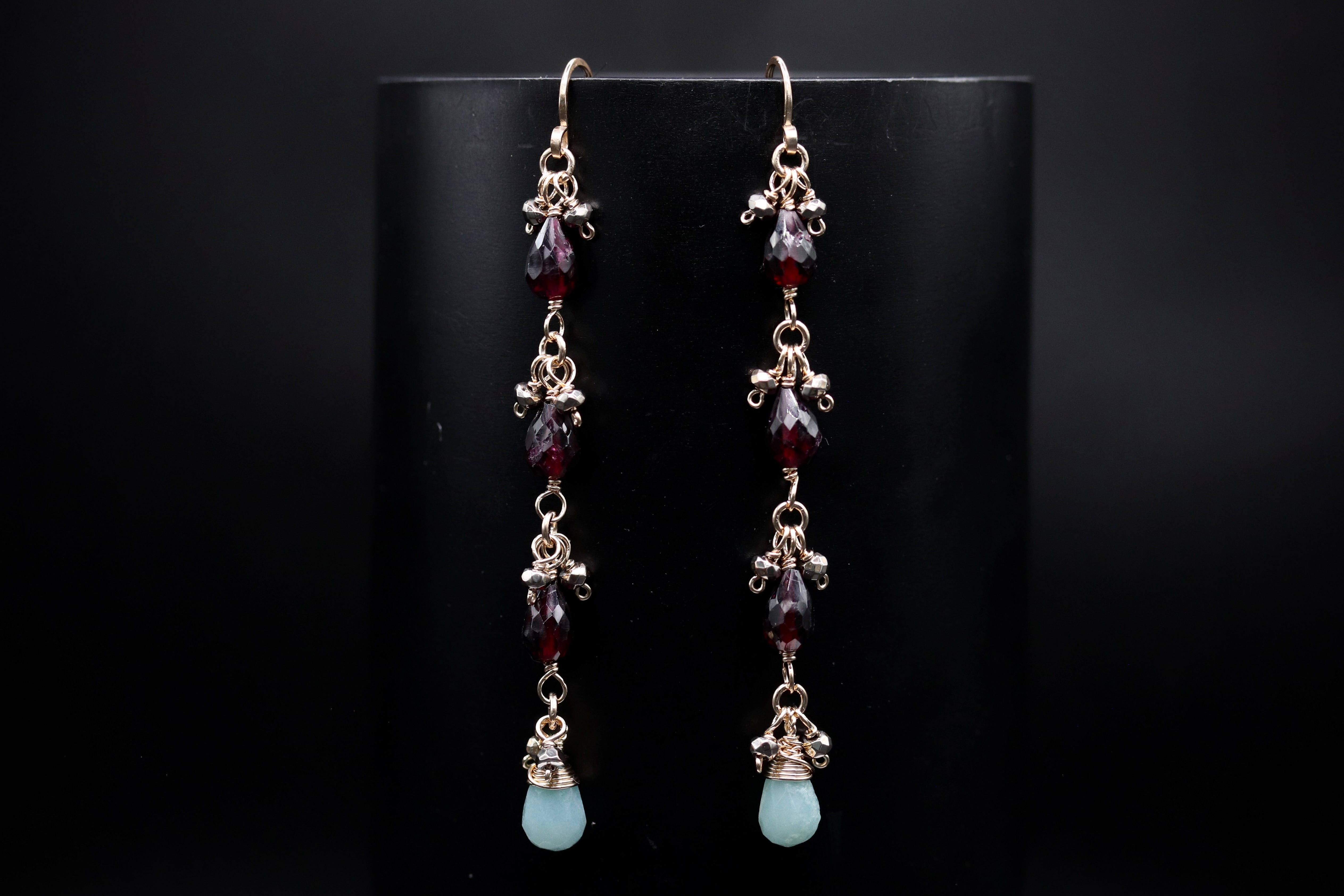 A pair of elegant earrings with dangling gemstone beads and metal accents, displayed against a dark background.