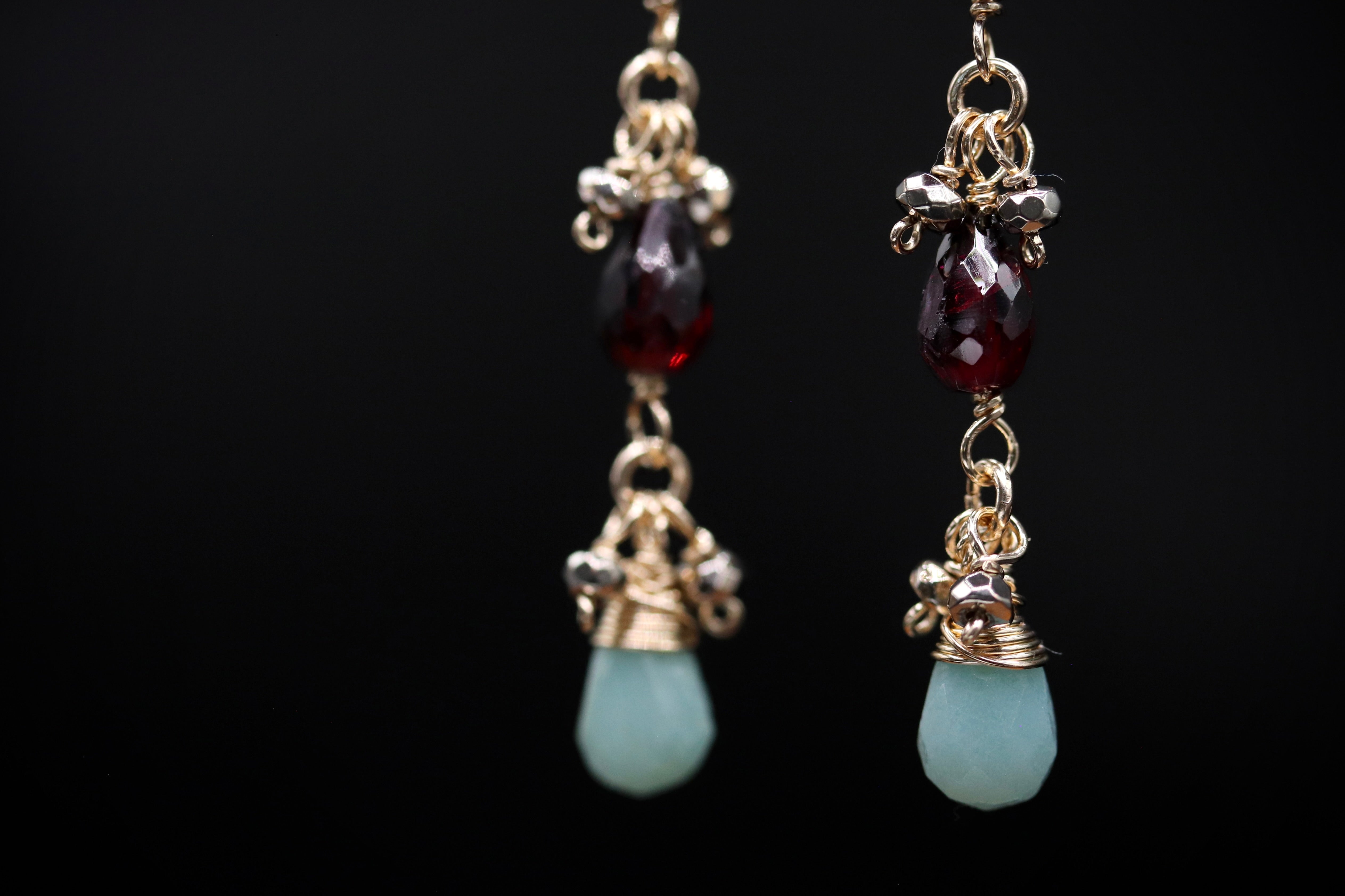 A pair of elegant earrings with a combination of red and green gemstones, suspended from a chain with small metal charms.