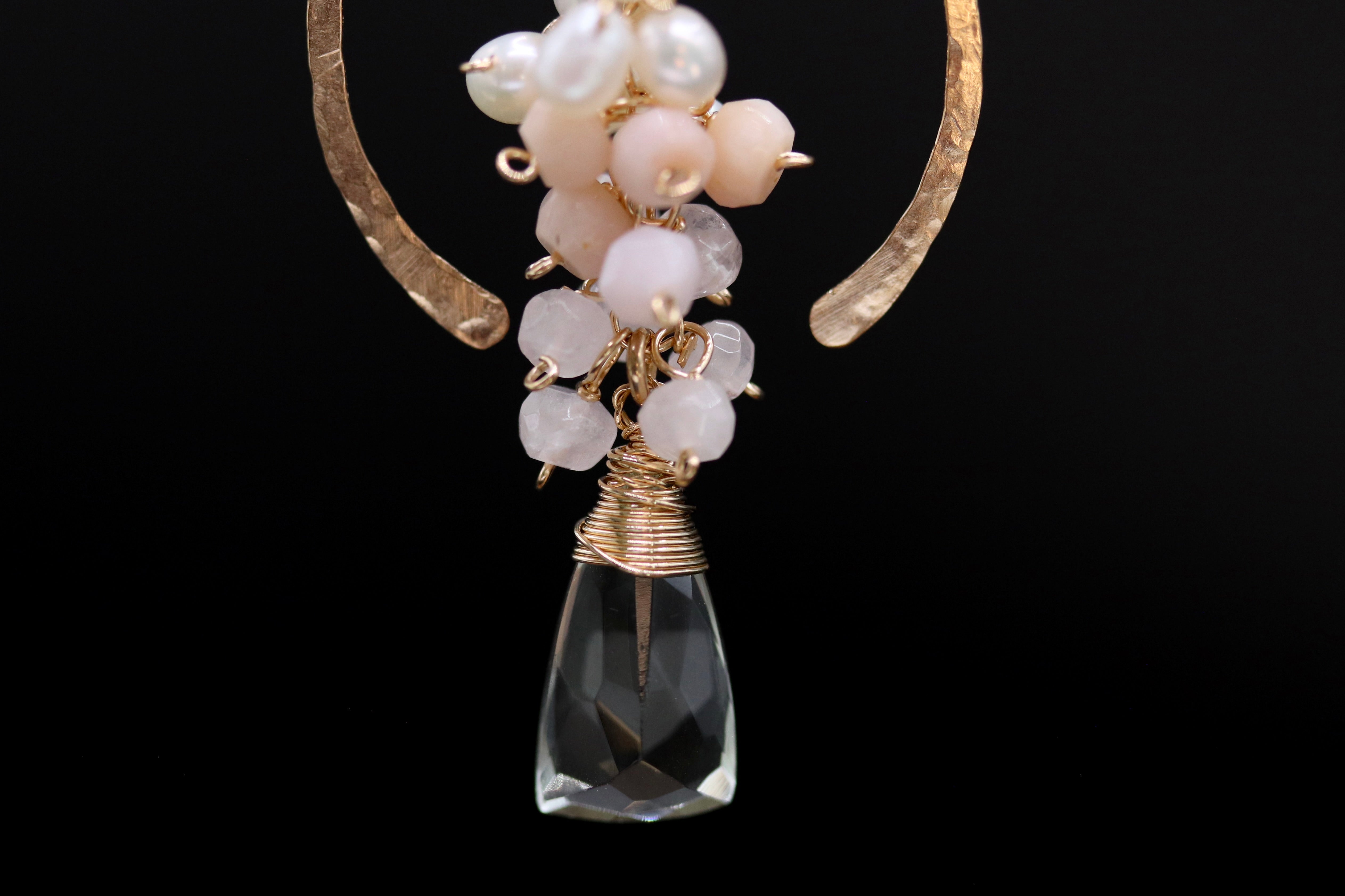 A close-up view of a clear crystal pendant with a twisted metal design and a cluster of small white and pink beads.