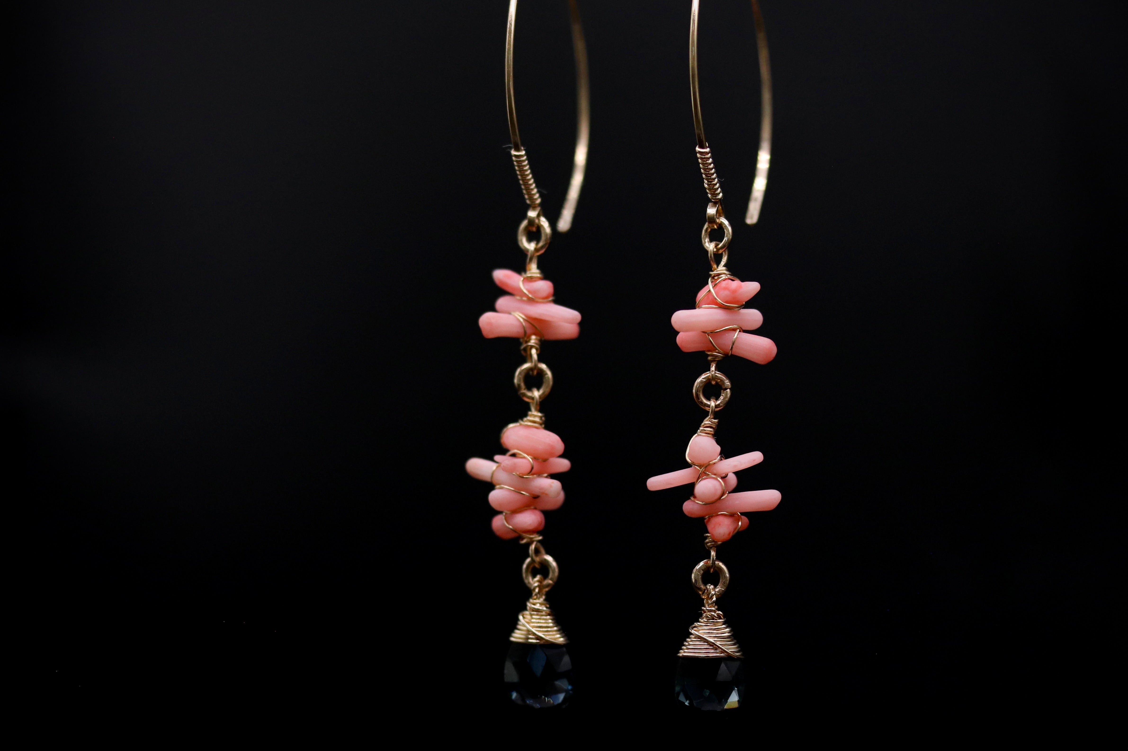 A pair of gold earrings with pink and black beads hanging from the bottom, set against a black background.
