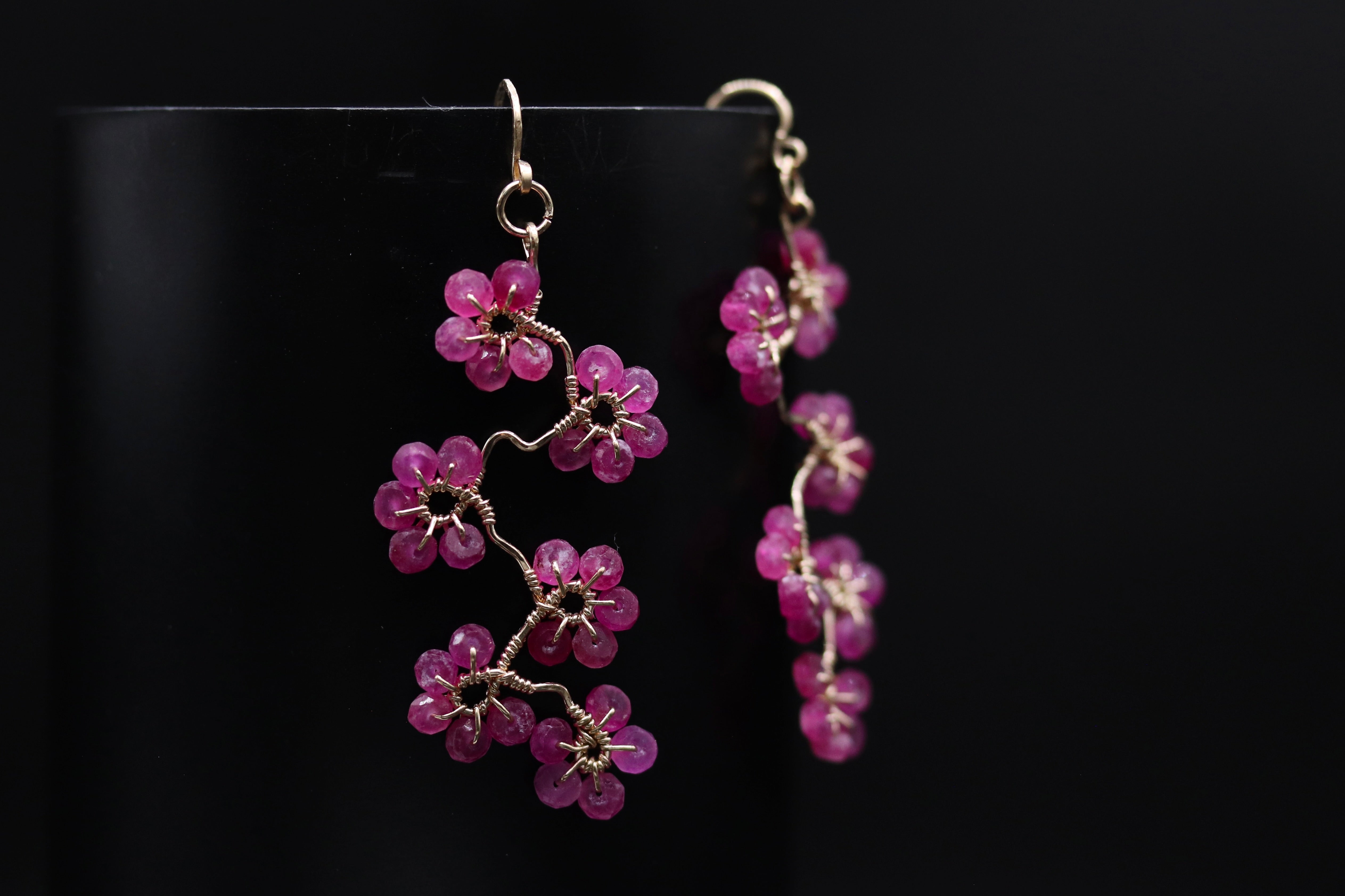 A pair of delicate earrings with small, vibrant pink flowers or branches hanging from a wire.
