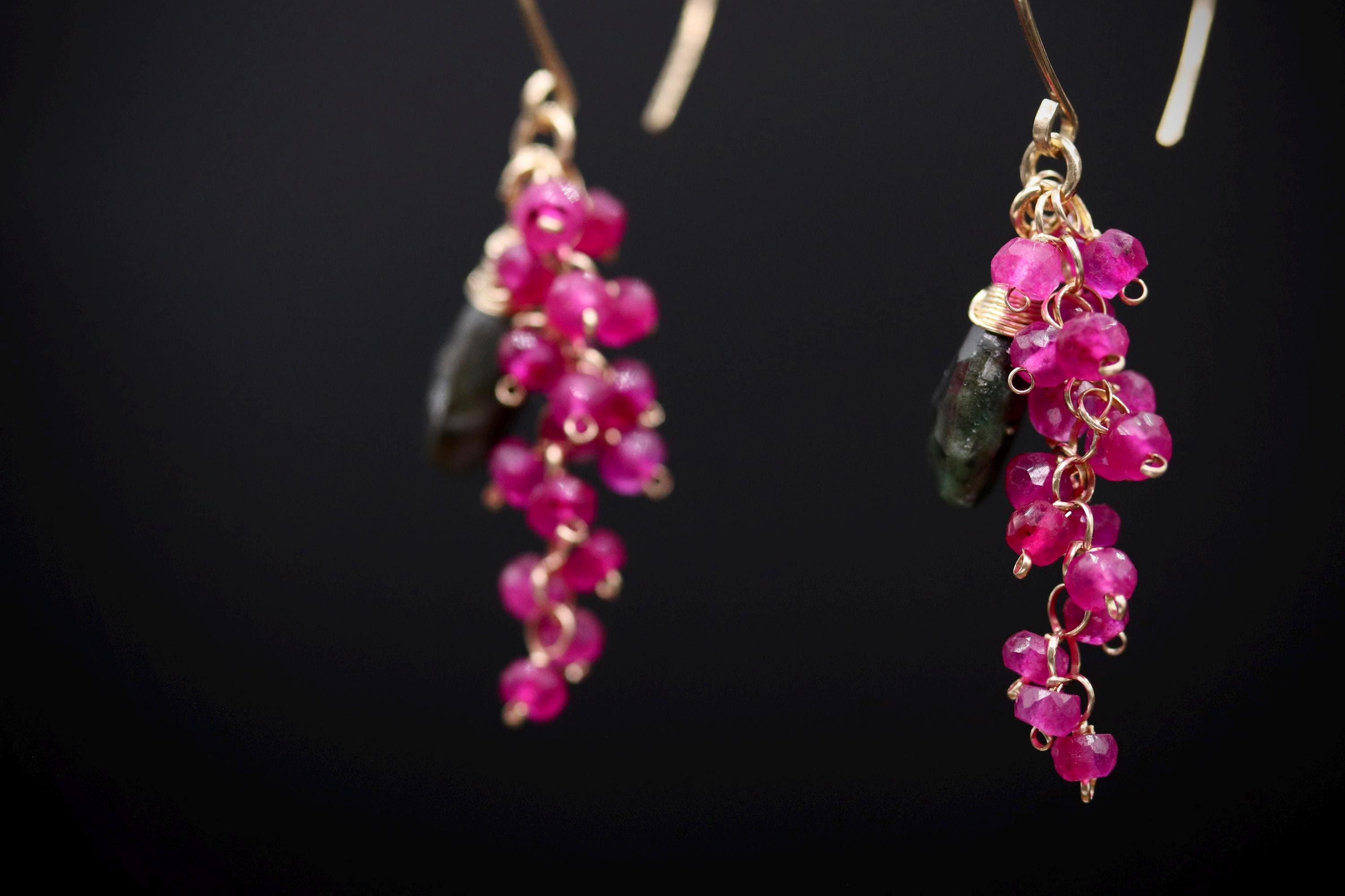 A pair of earrings with a combination of pink and green gemstones, hanging against a dark background.