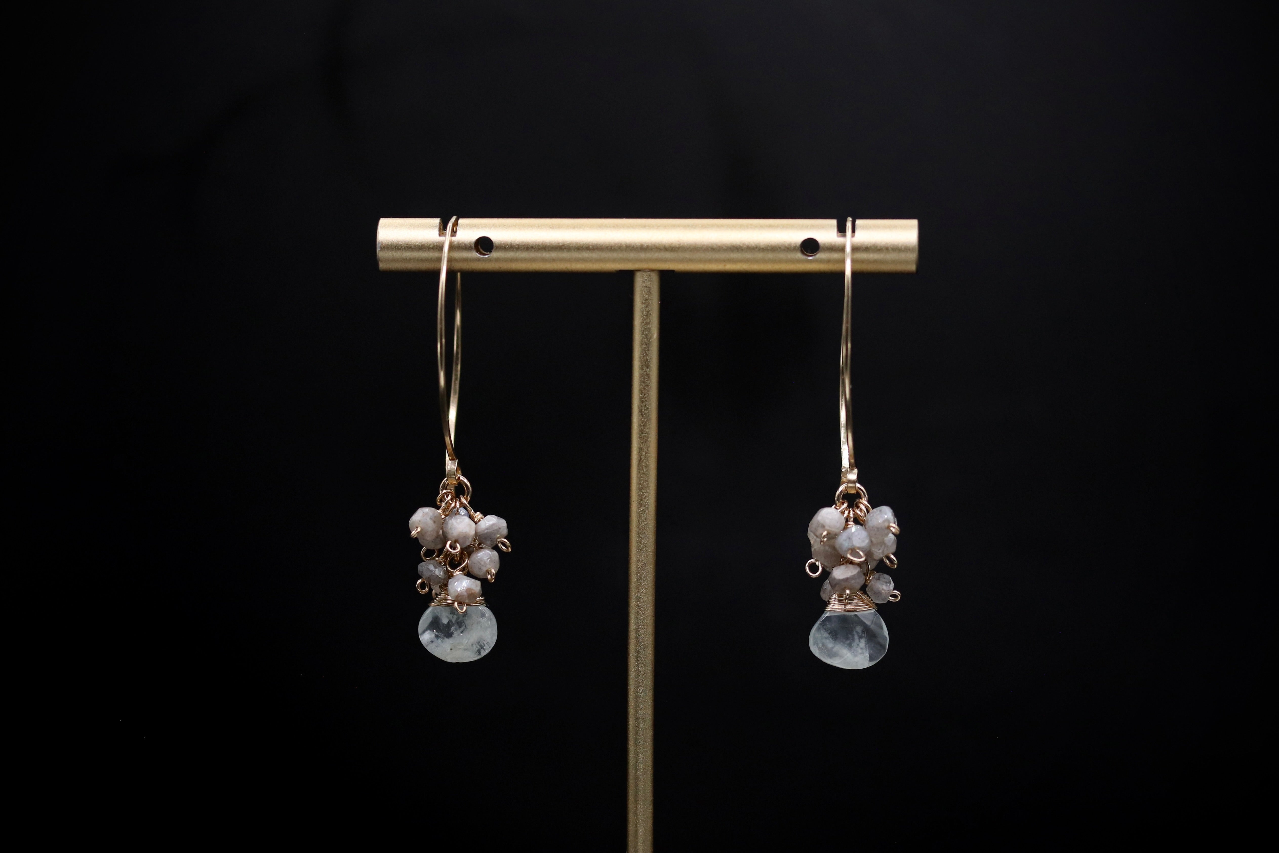 A pair of gold earrings with white stones hanging from them, displayed on a gold stand against a black background.
