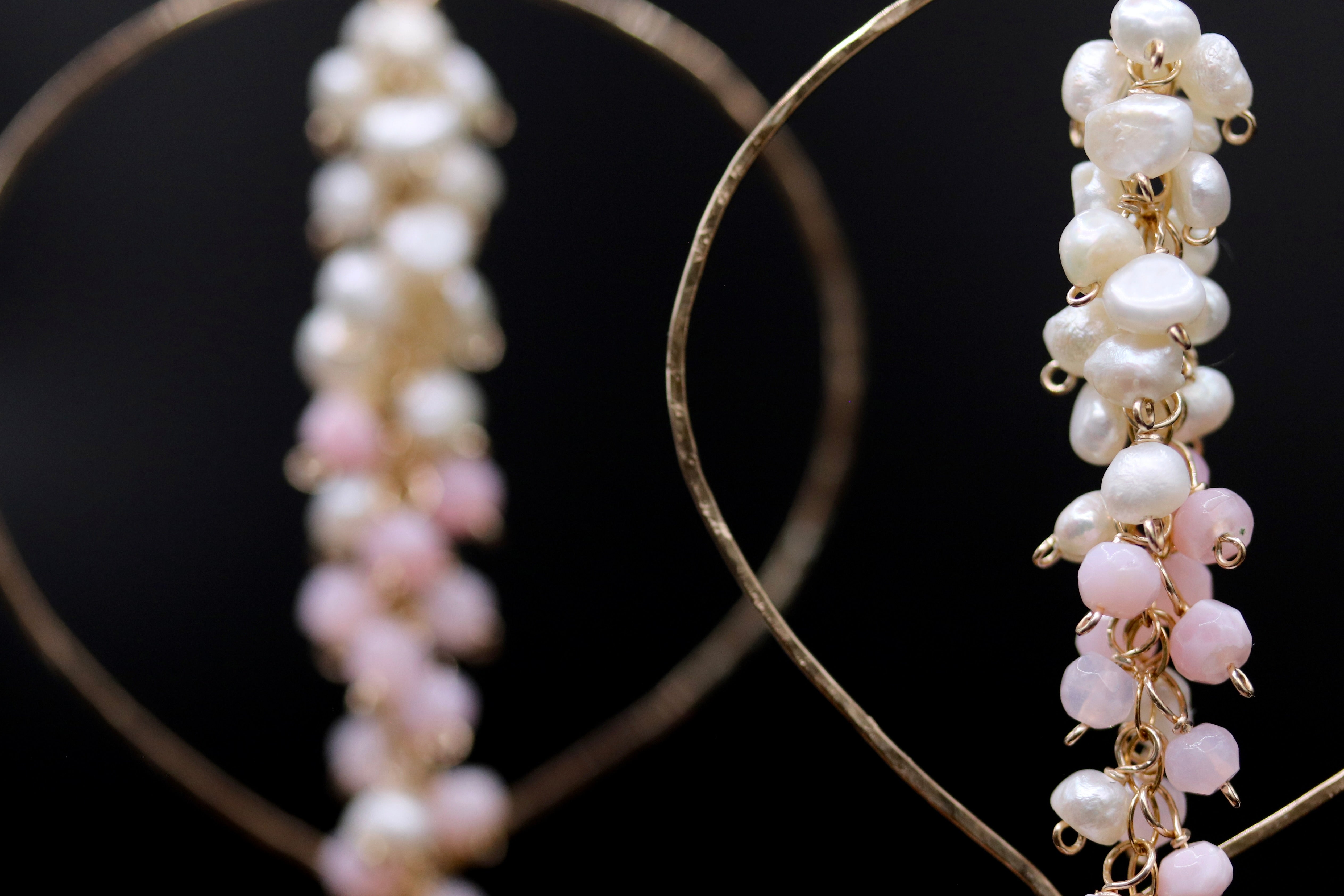 A close-up view of a pair of earrings with a combination of white and pink pearls and small beads, set against a dark background.