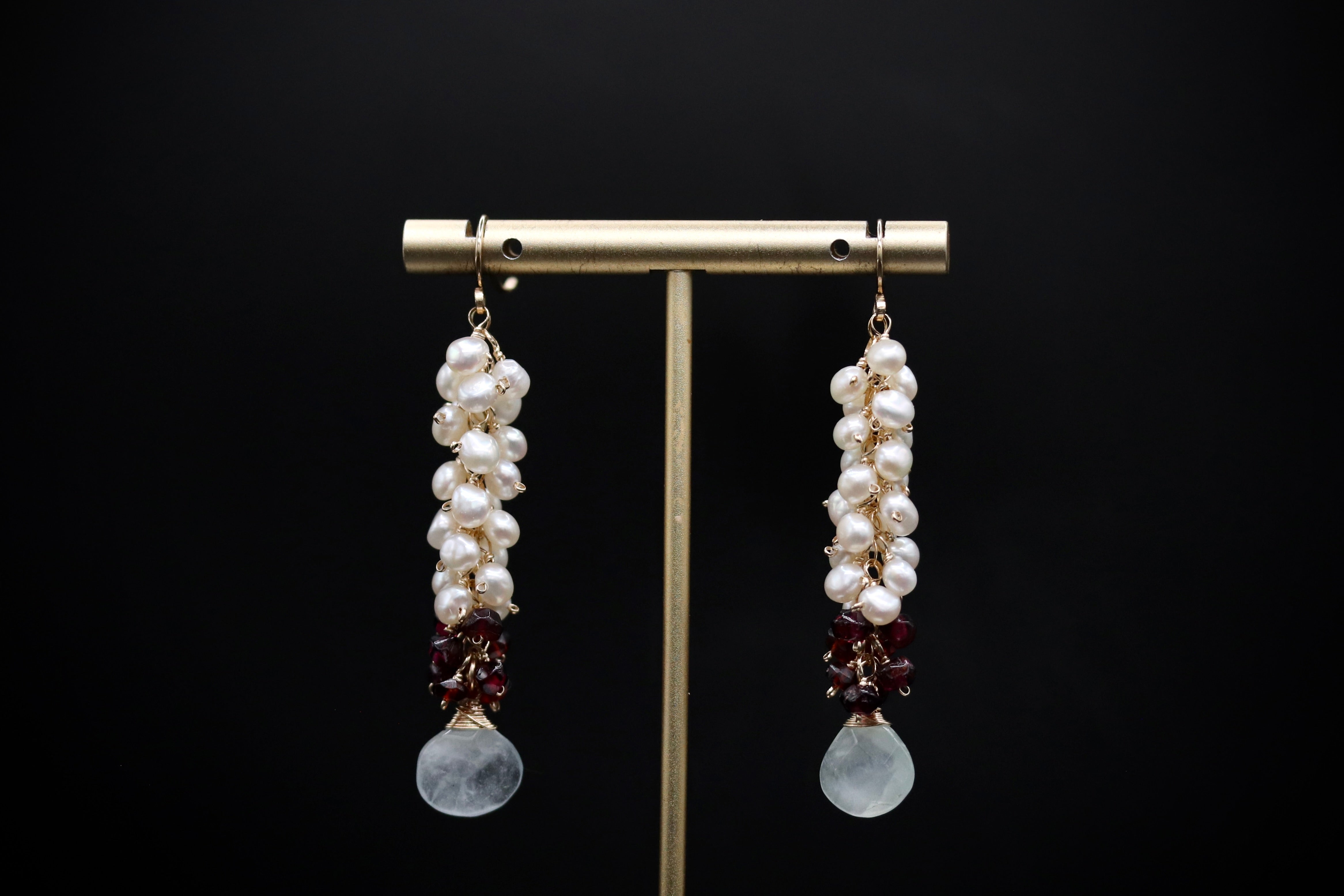 A pair of elegant earrings with white pearls, red garnishes, and white stones hanging from the bottom.