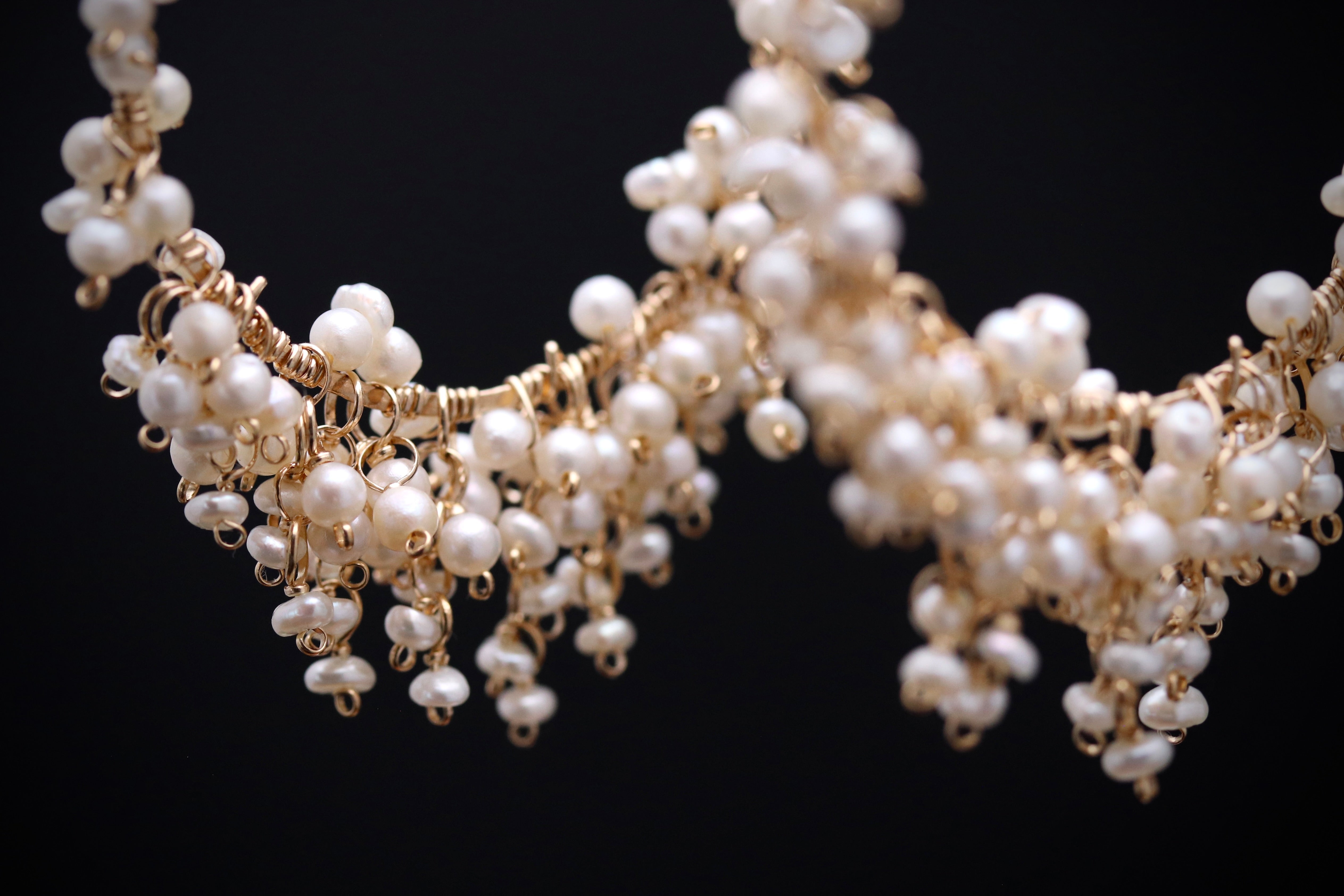 A close-up view of a delicate, ornate necklace made of small, white pearls and gold wire.