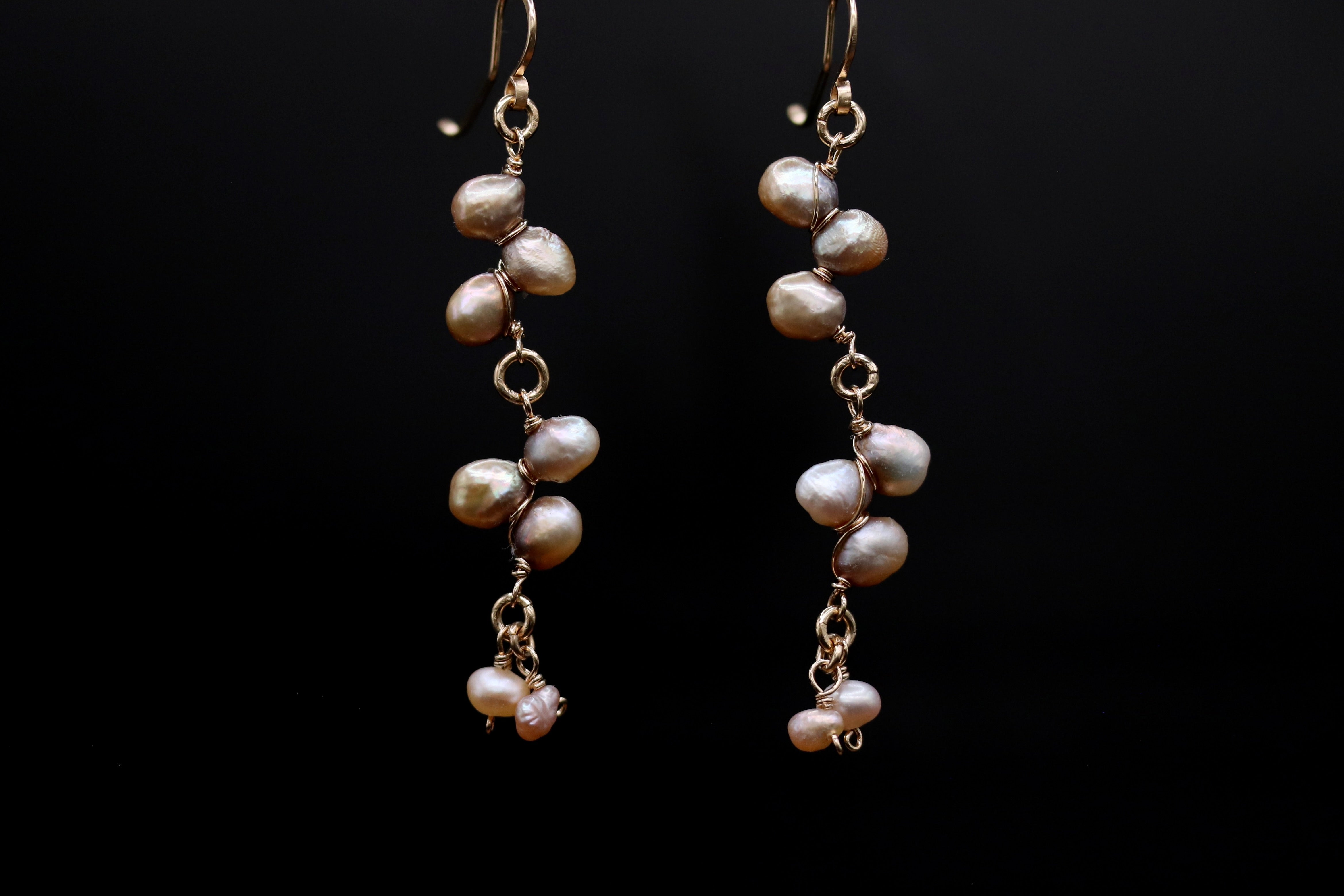A pair of elegant earrings with a delicate design, featuring a cluster of small, round pearls suspended from a thin, gold-colored metal hook.