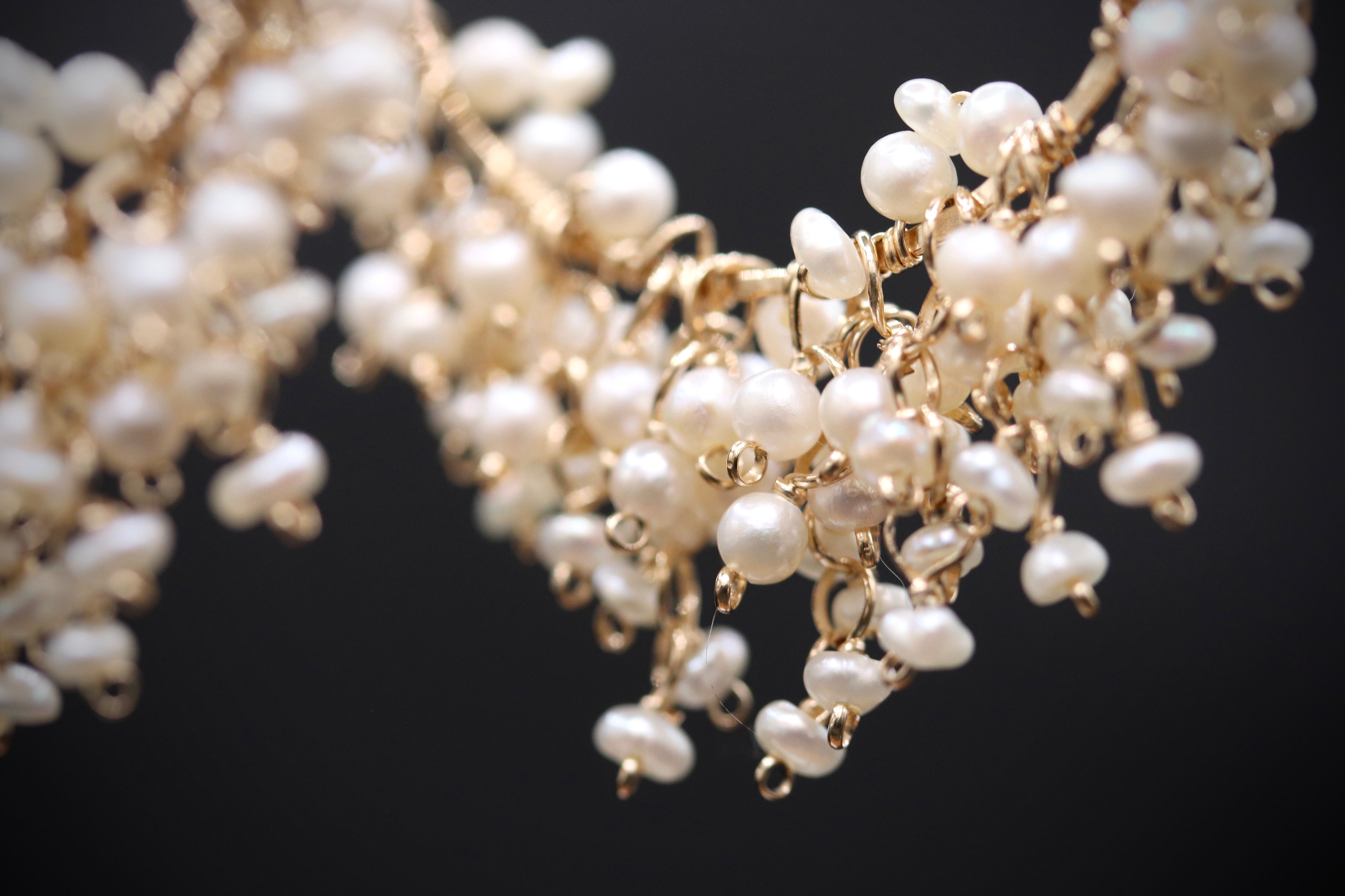A close-up view of a delicate, intricate necklace made of small, white pearls strung together with gold wire.