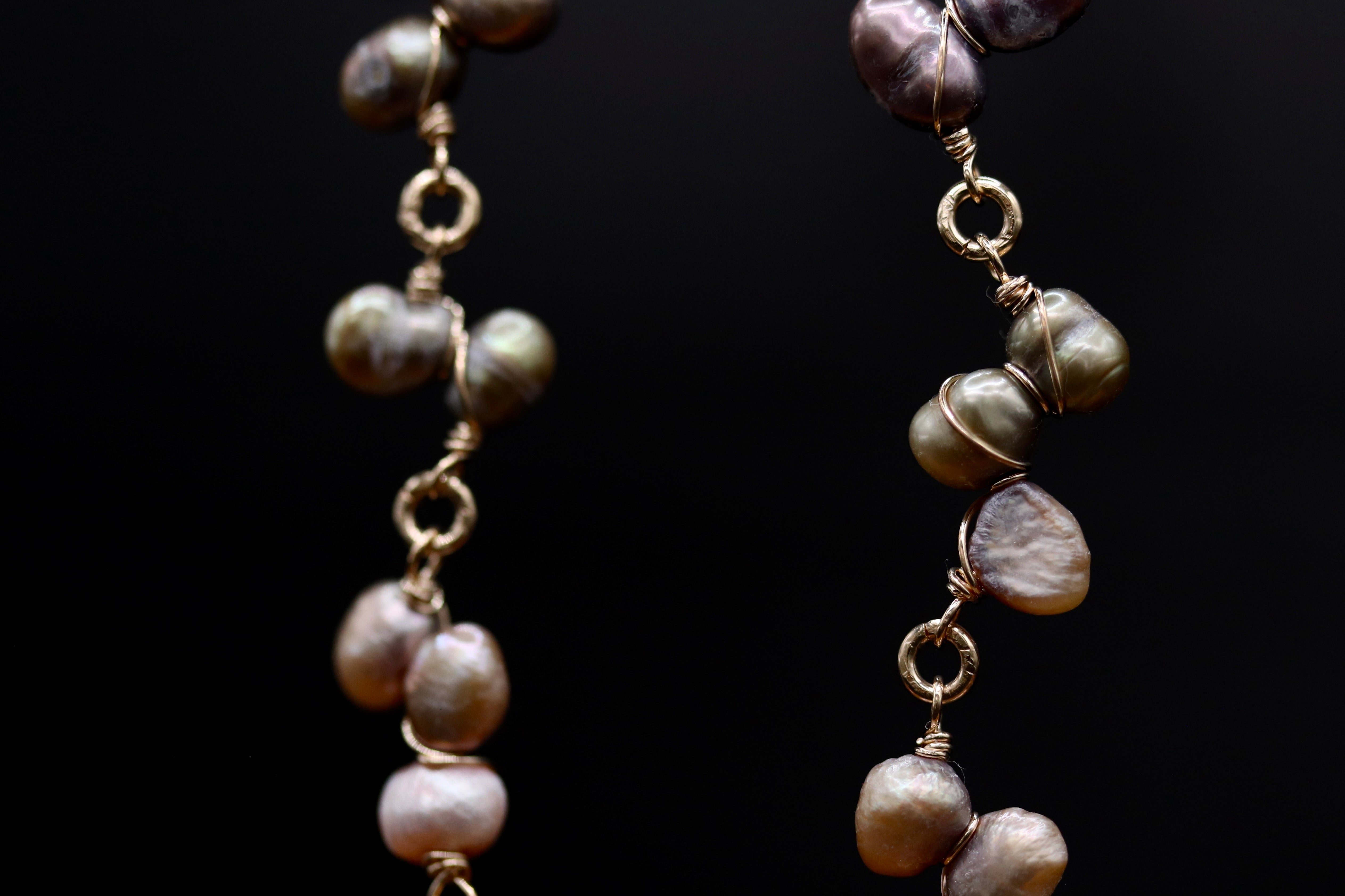 A close-up view of a necklace with multiple strands of pearls and gold-colored metal chains against a dark background.