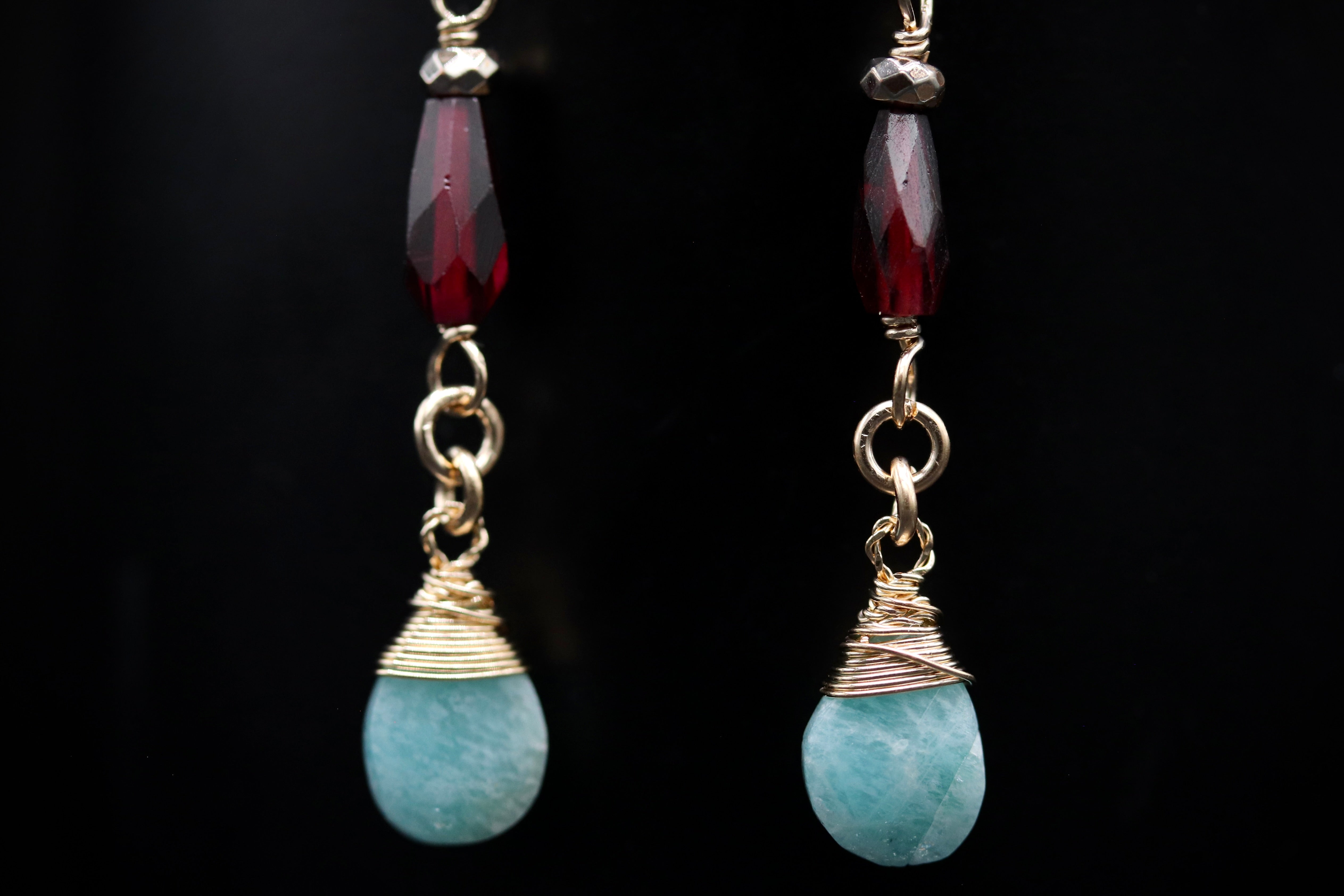 A pair of earrings with turquoise stones and red gemstones, suspended from gold chains against a black background.