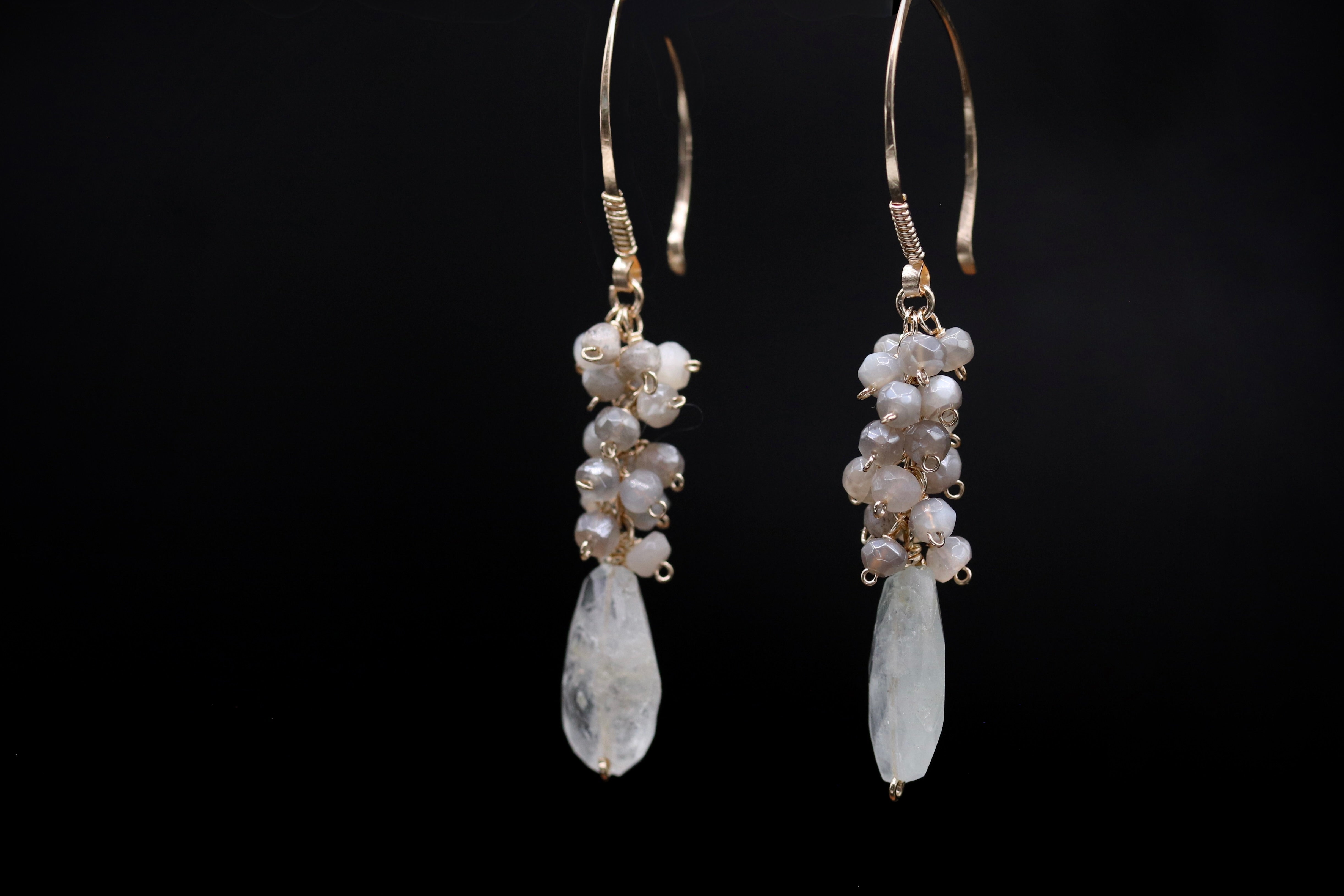 A pair of elegant earrings with white stones and gold accents, displayed against a black background.