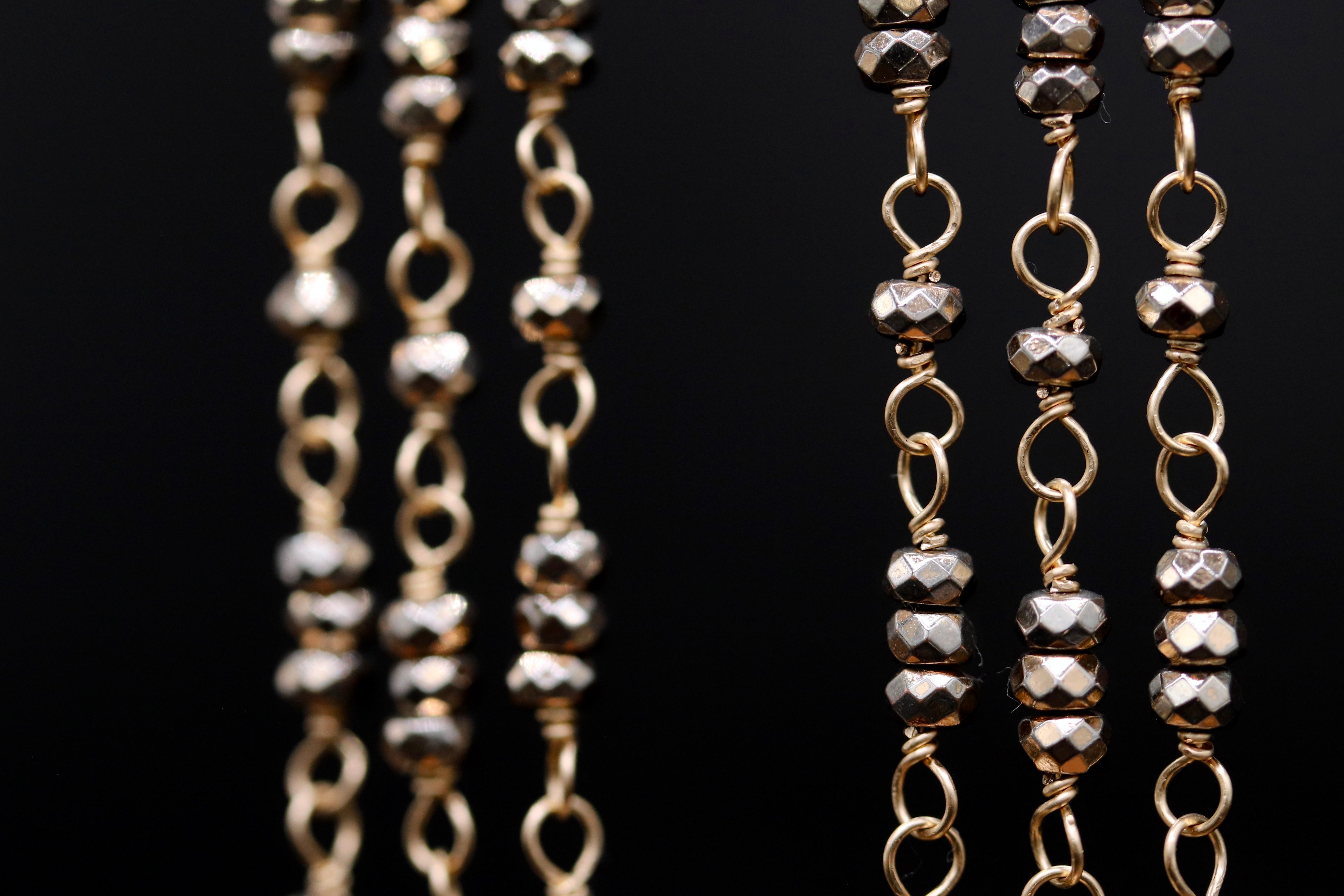A close-up view of a collection of gold-colored metal beads and chains against a black background.