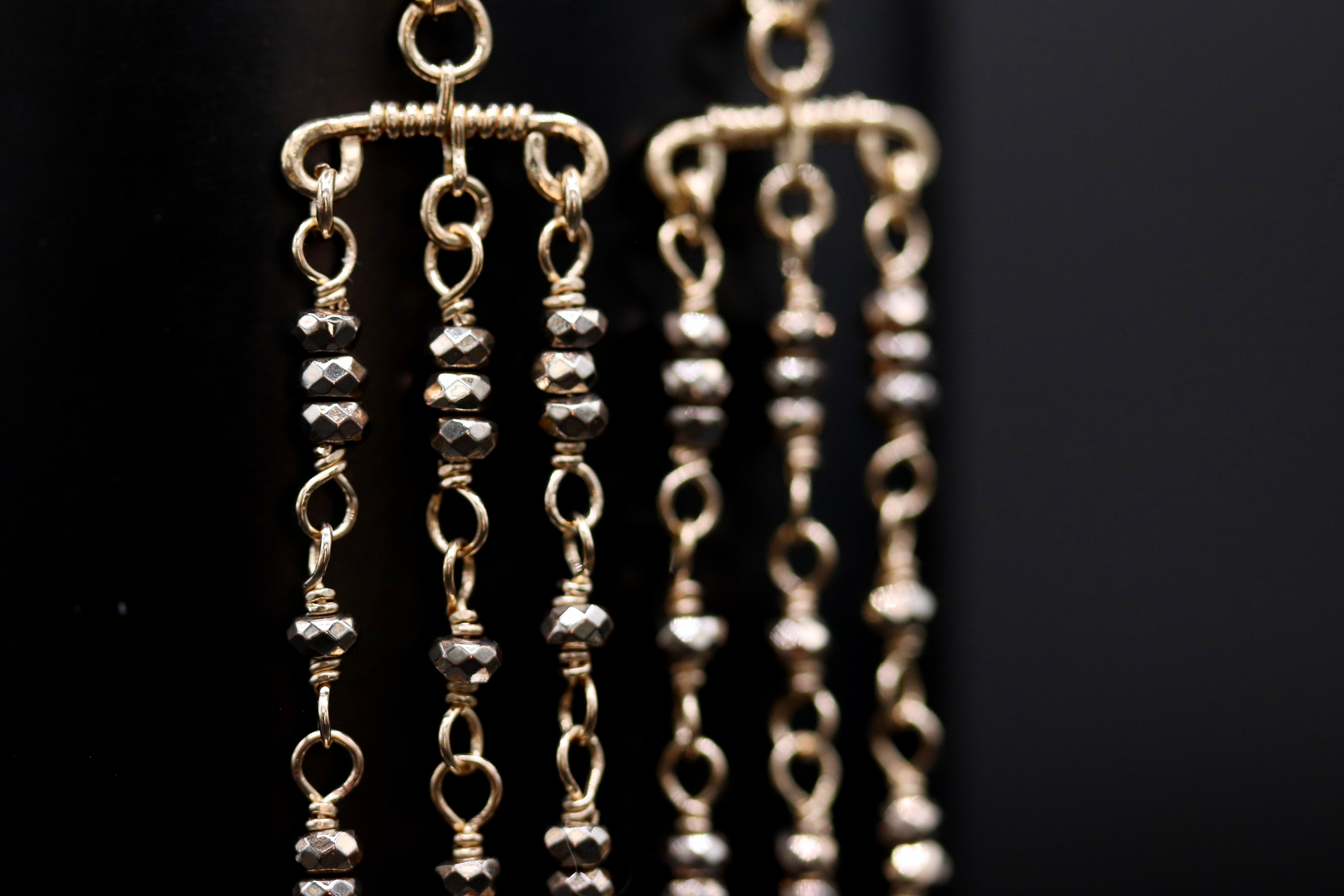 A close-up view of a pair of gold-colored earrings with multiple tiers of small, dangling beads.