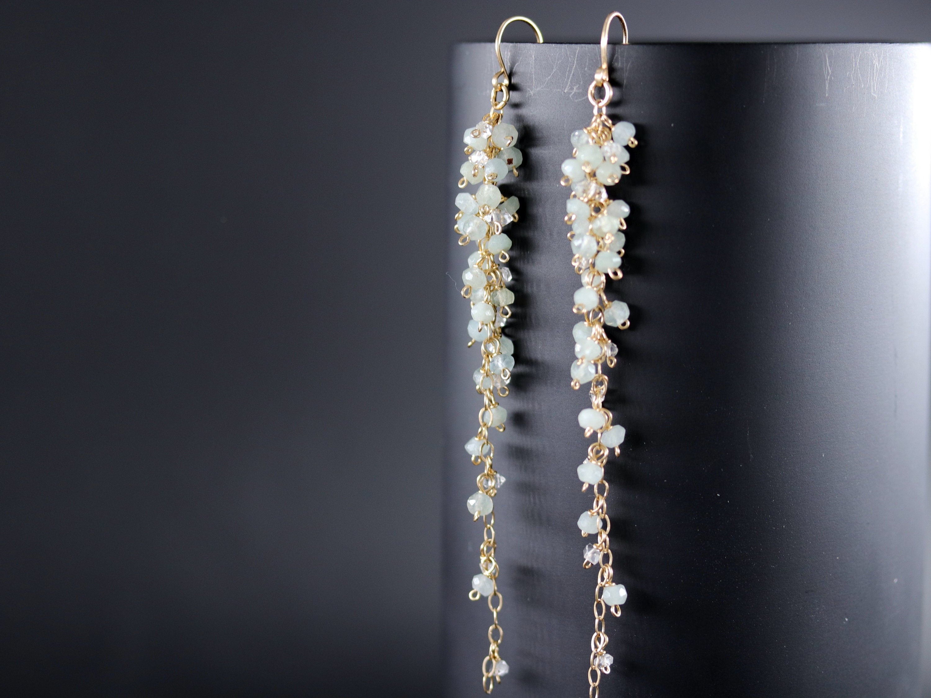 May include: A pair of long, delicate earrings with a cascading design. The earrings are made of gold chain and small, light green gemstones.