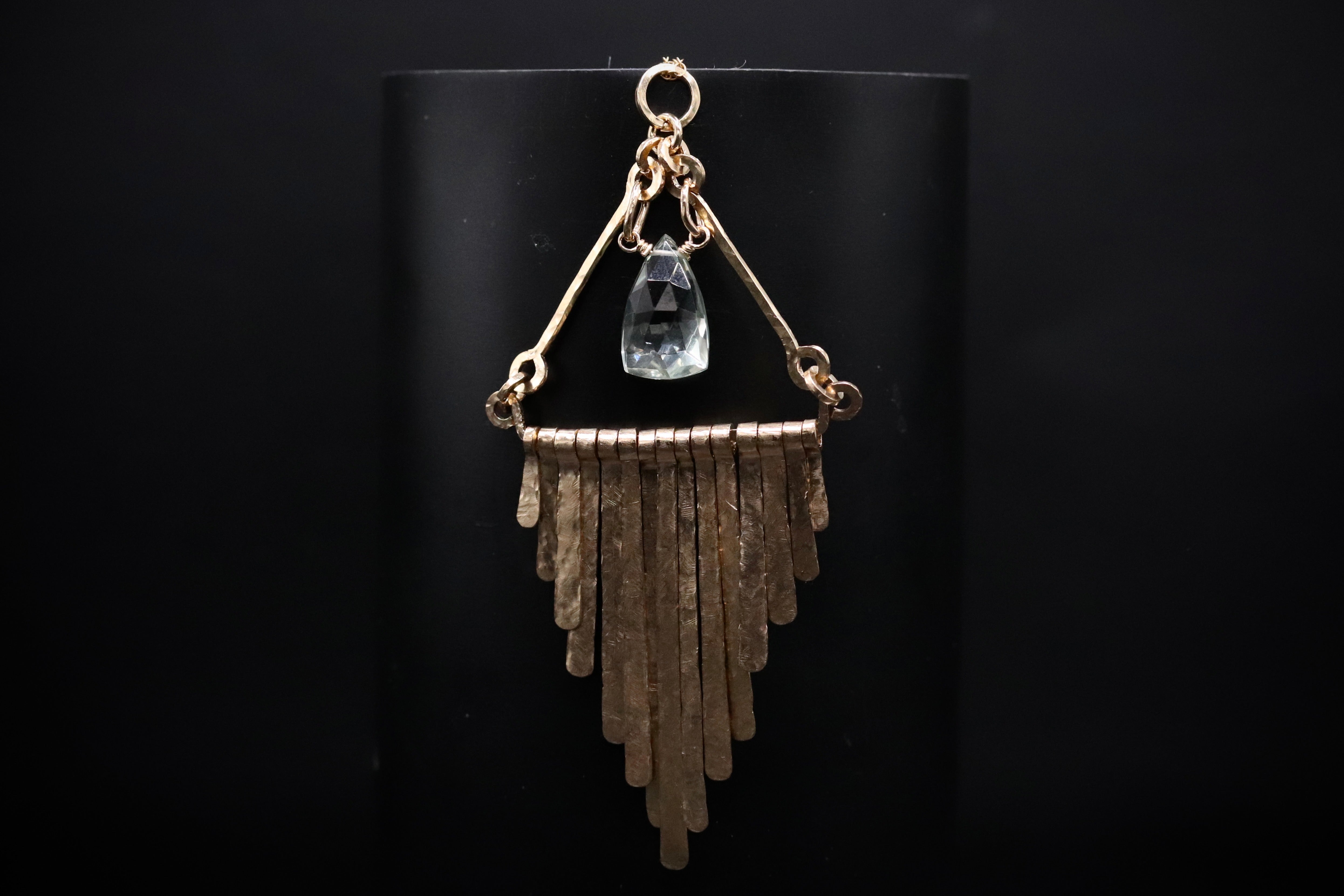 A gold-colored necklace with a clear gemstone pendant and a dangling metal element.