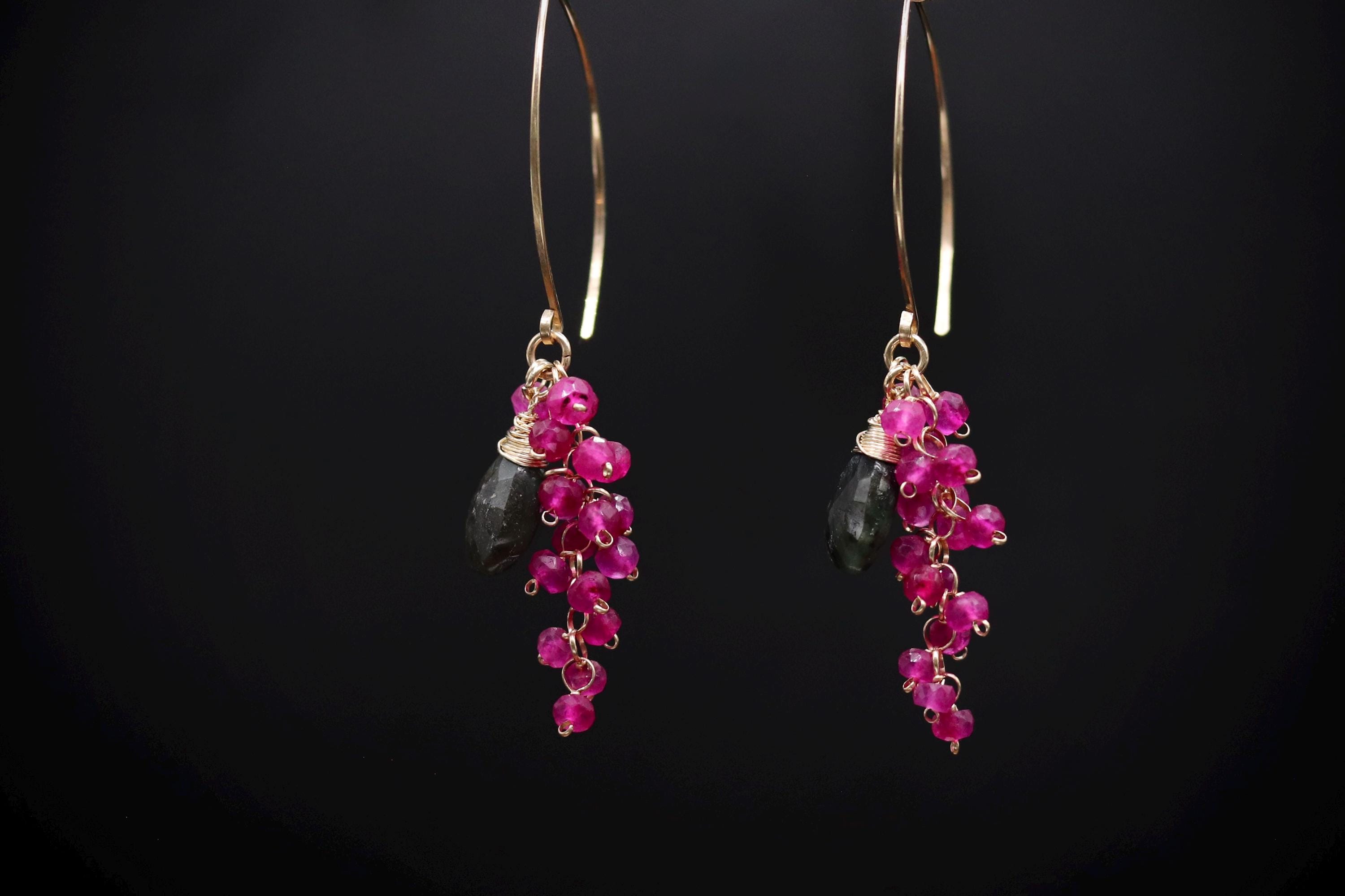 A pair of gold hoop earrings with a combination of pink and black gemstones hanging from them against a black background.