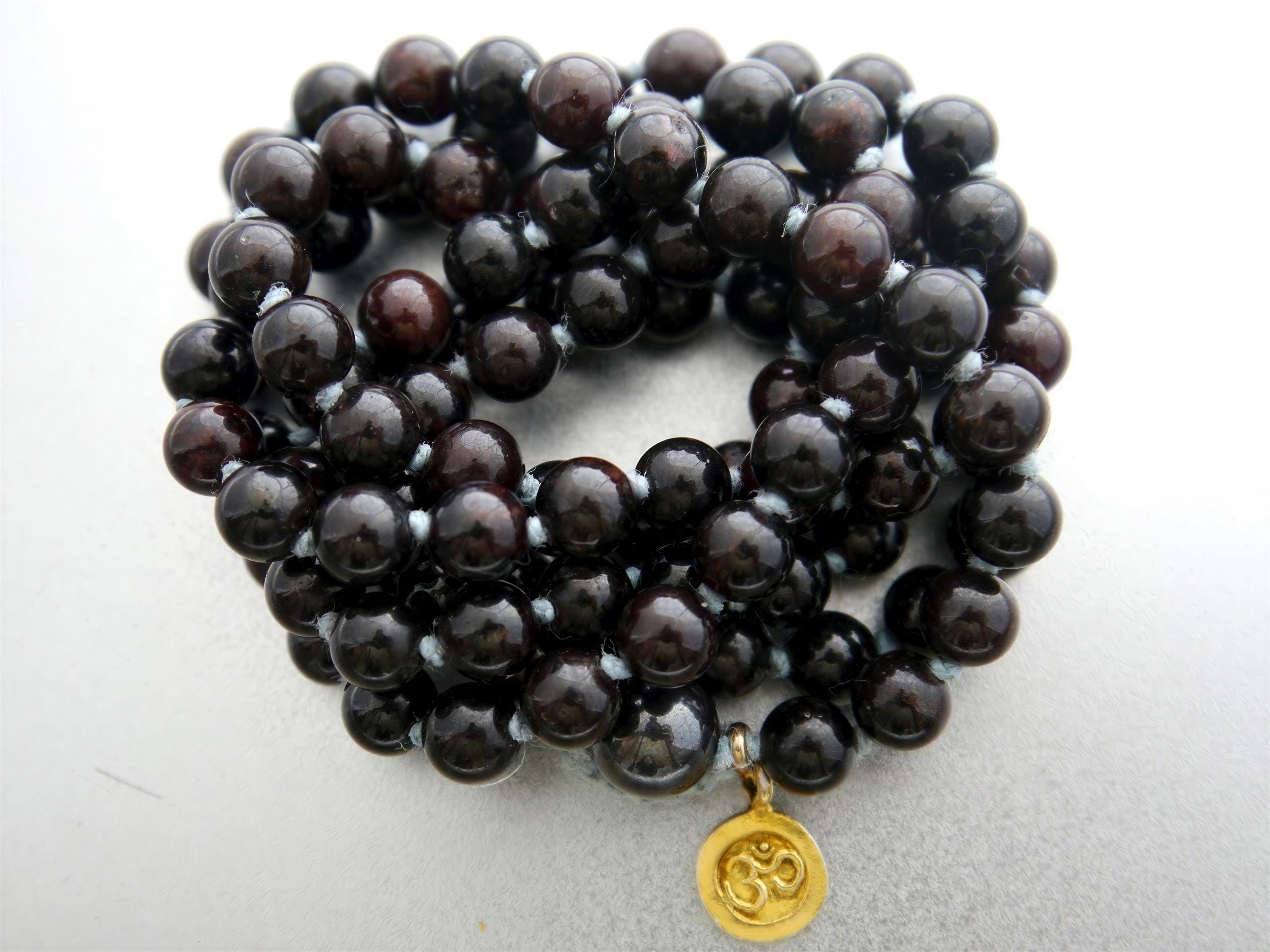 A close-up image of a beaded bracelet with dark brown beads, and a gold pendant with an Om symbol.
