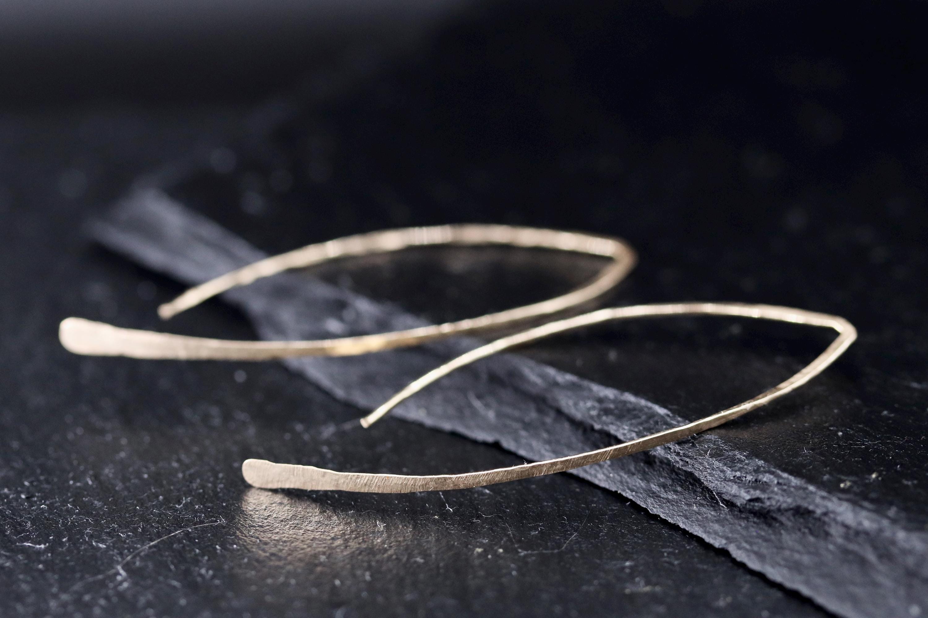 A pair of gold earrings with a textured, metallic appearance rests on a dark surface.