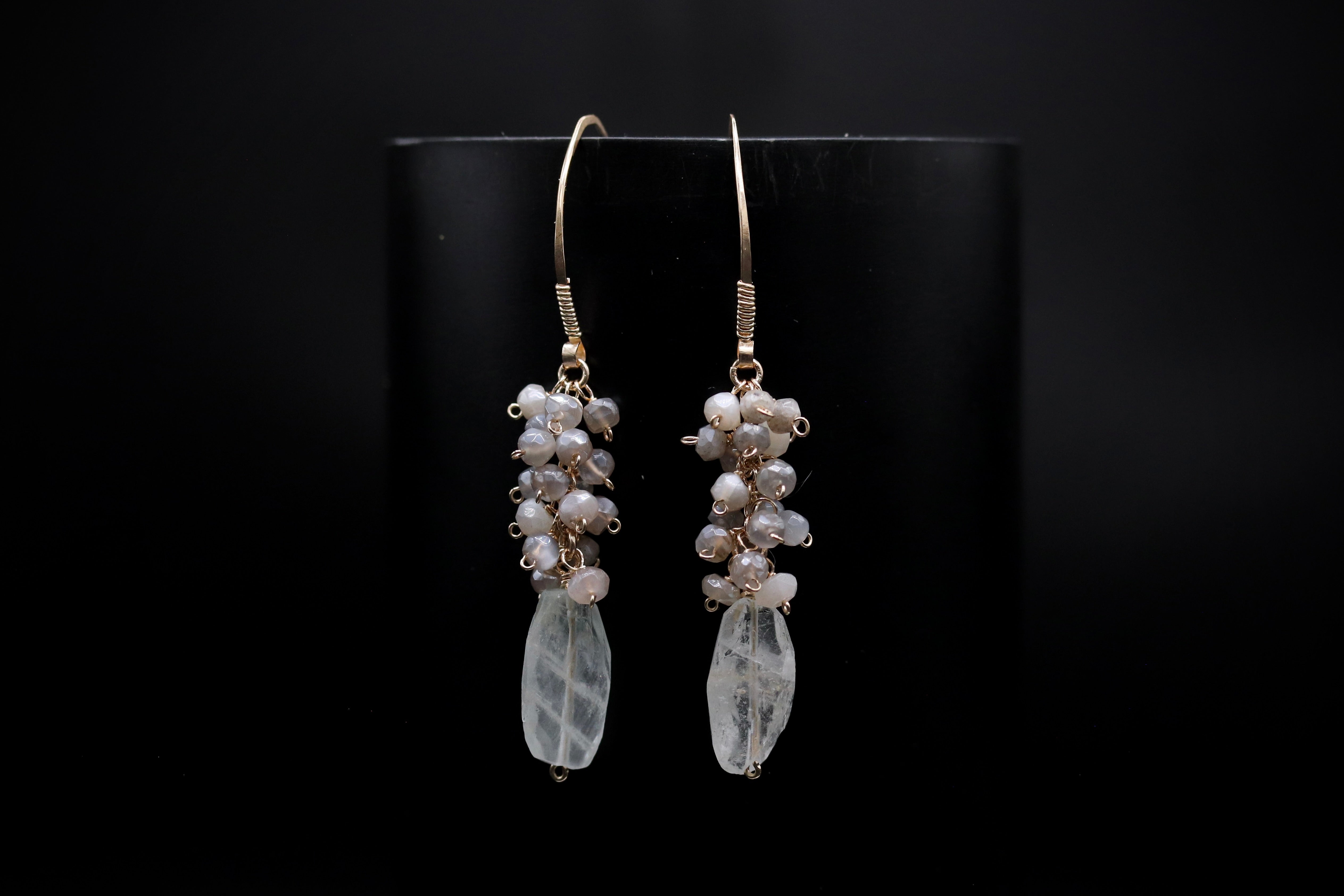 A pair of elegant earrings with clear crystal pendants and dangling pearl-like stones against a black background.