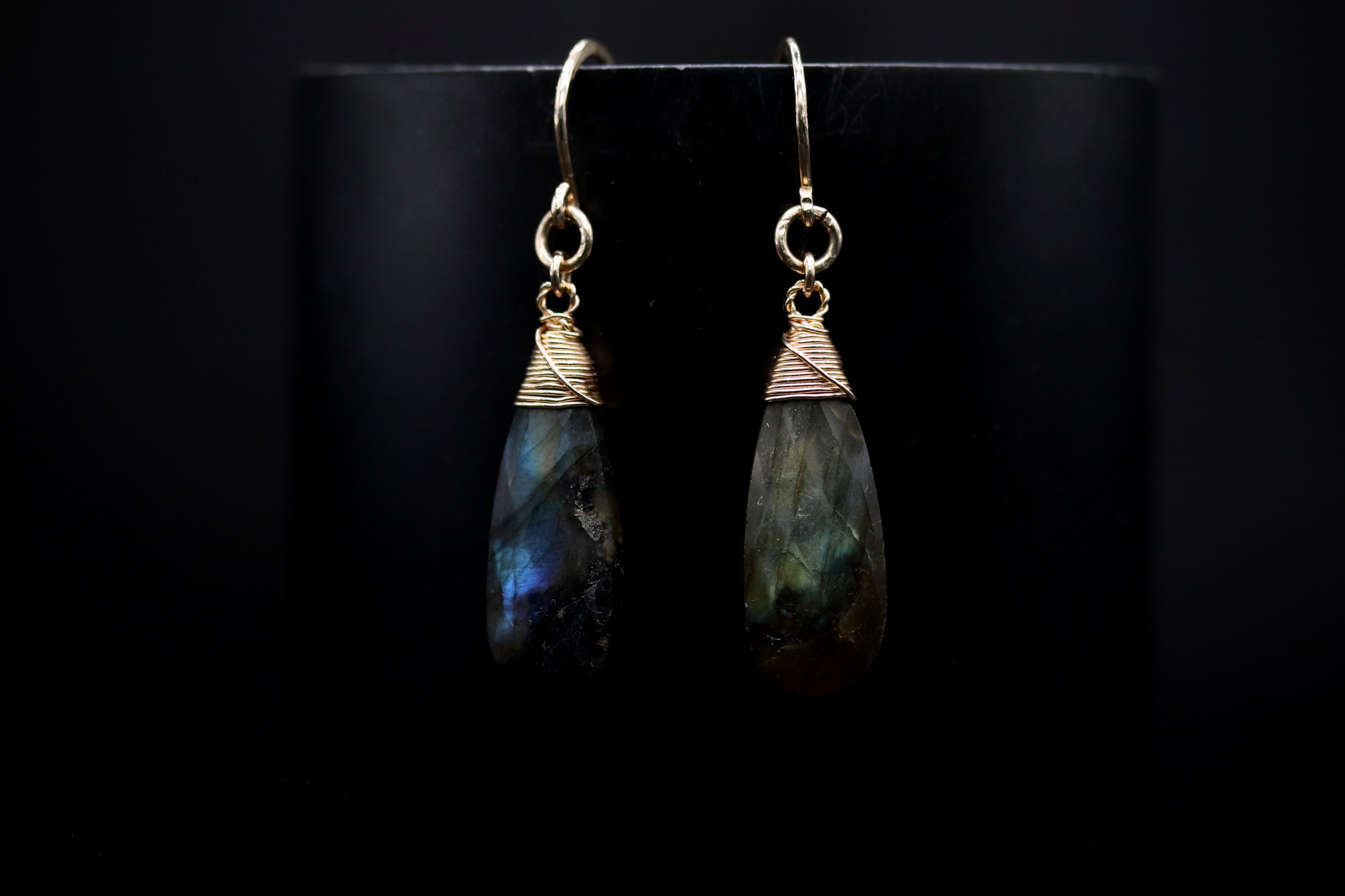 A pair of elegant earrings with a dark stone pendant, displayed against a black background.