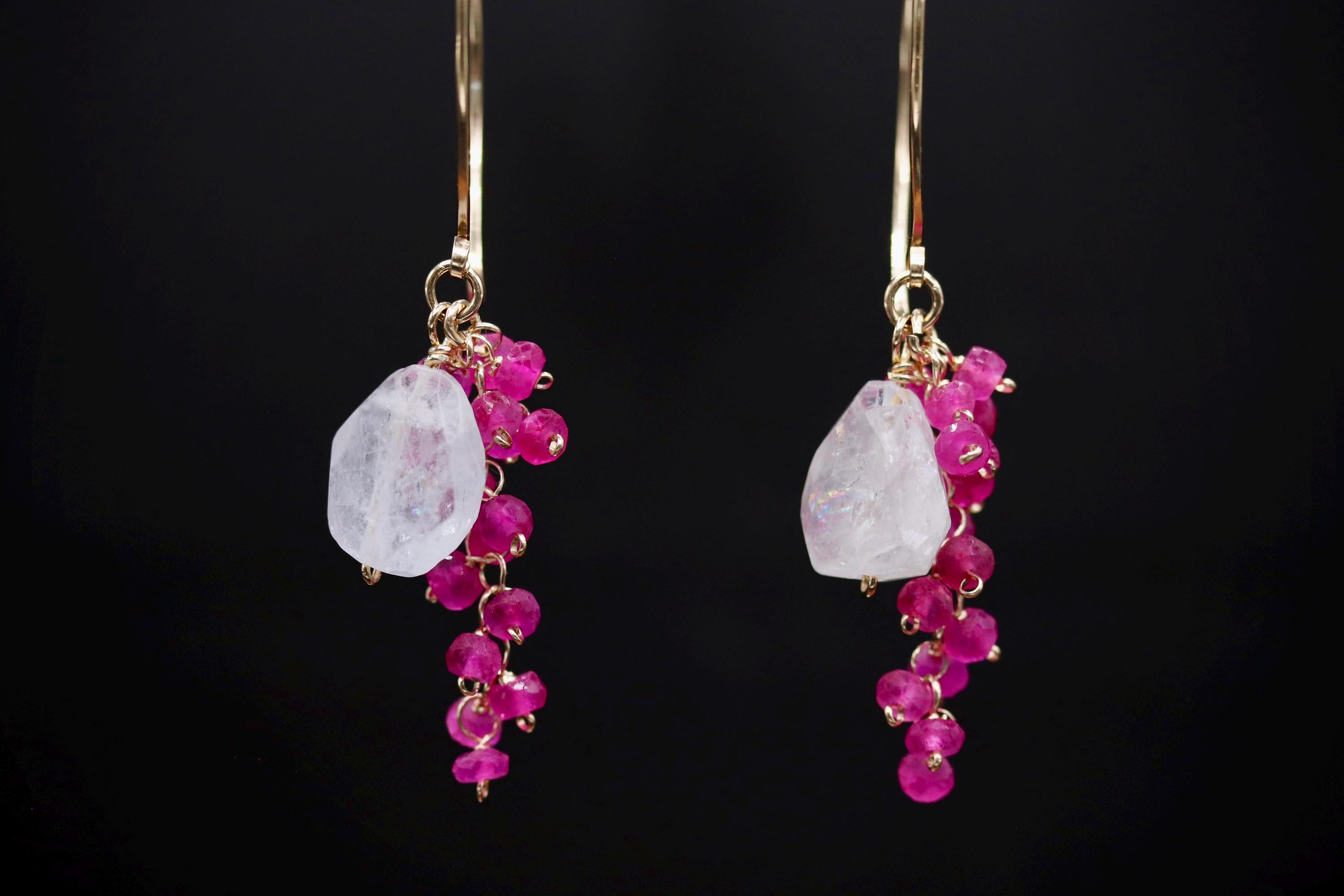 A pair of elegant earrings with a combination of white and pink gemstones, as well as small, dangling beads in a vibrant shade of pink.