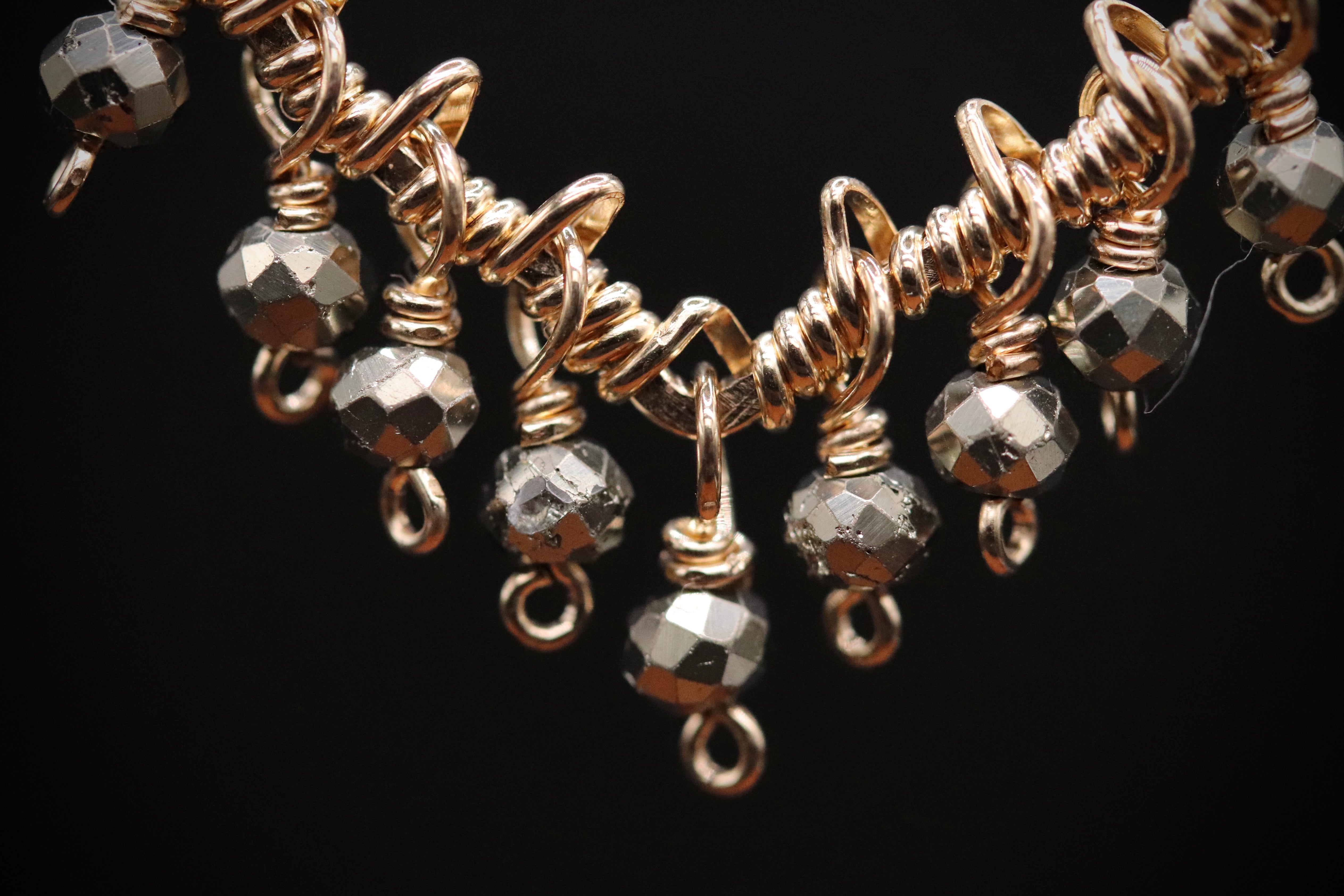 A close-up view of a gold-colored necklace with a series of small, round beads hanging from it against a black background.