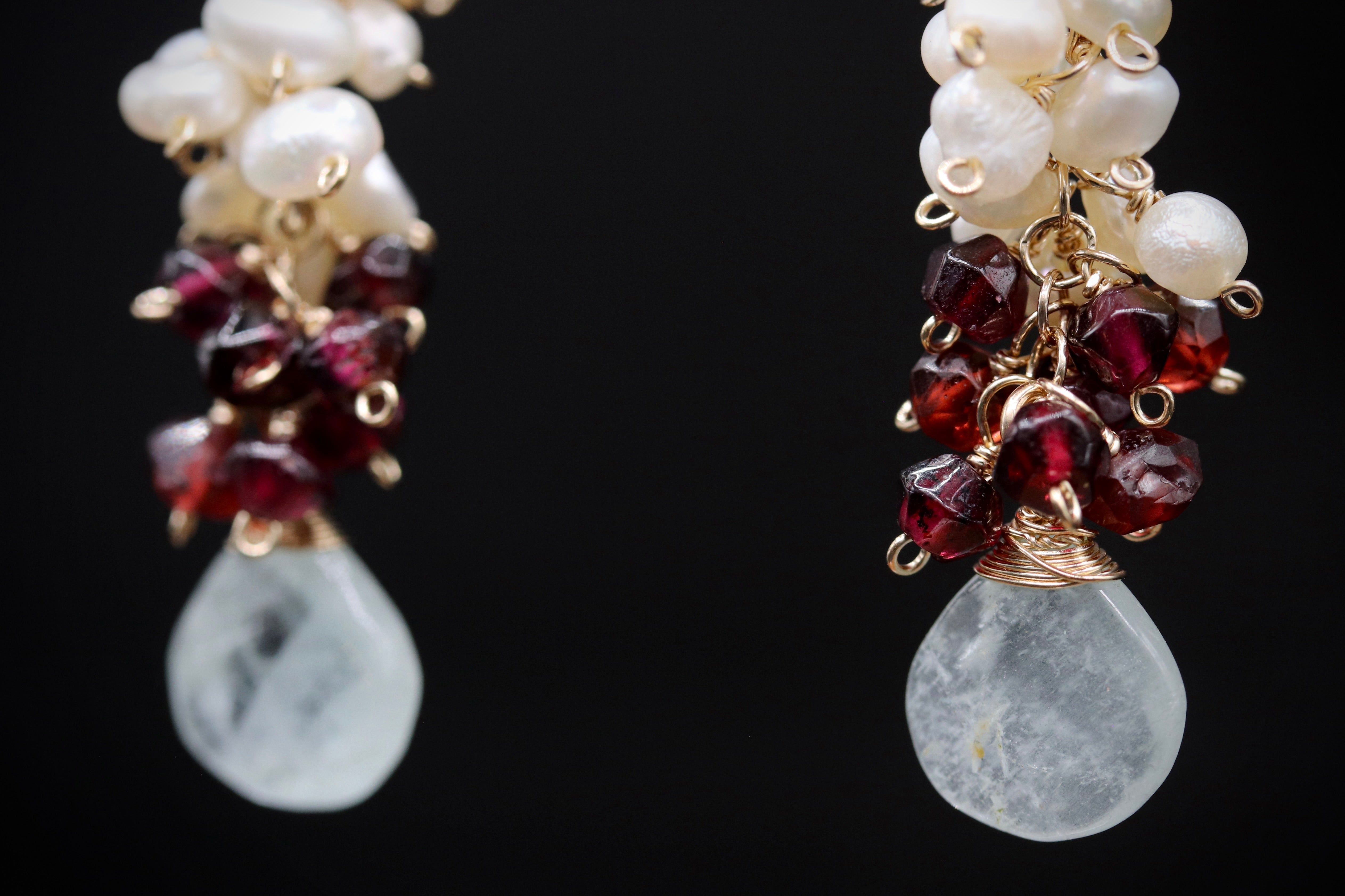 A pair of elegant earrings with white pearls and red garnets hanging from the ends.