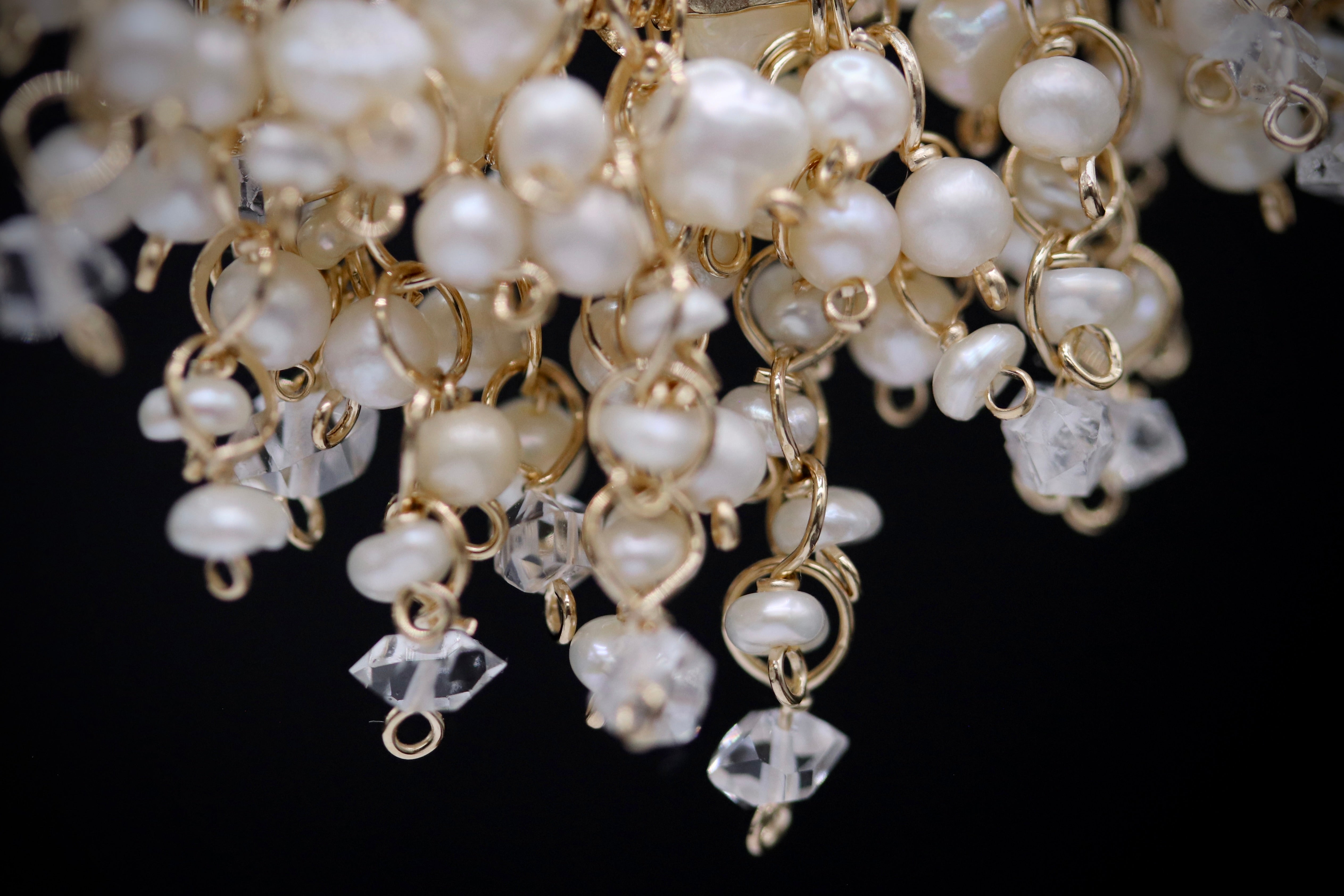 A close-up view of a delicate and intricate beaded necklace or bracelet, with numerous small white pearls and clear gemstones or crystals attached to the gold-colored metal links.