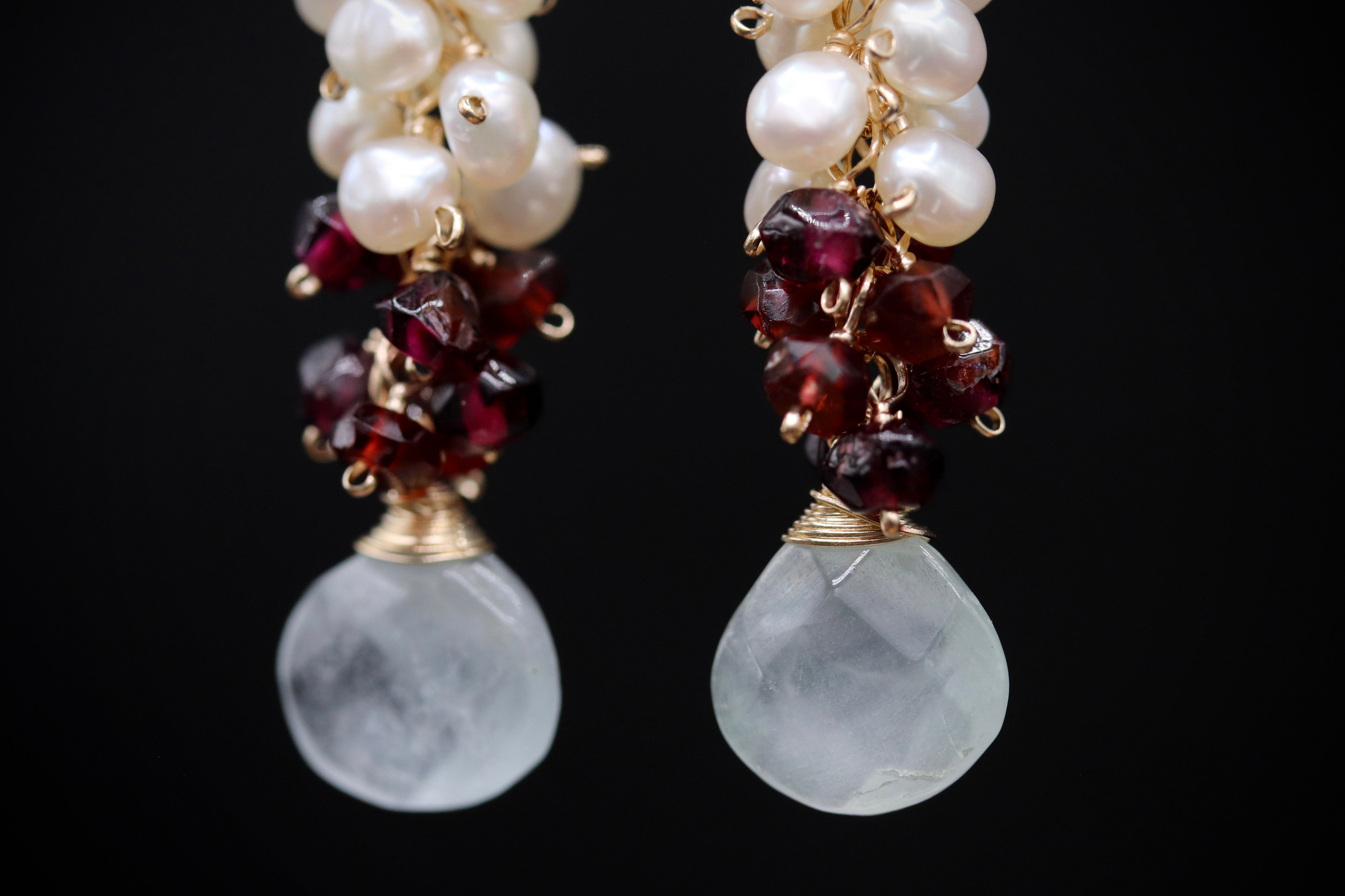 A pair of elegant earrings with white pearls and maroon garnets hanging from a gold chain.