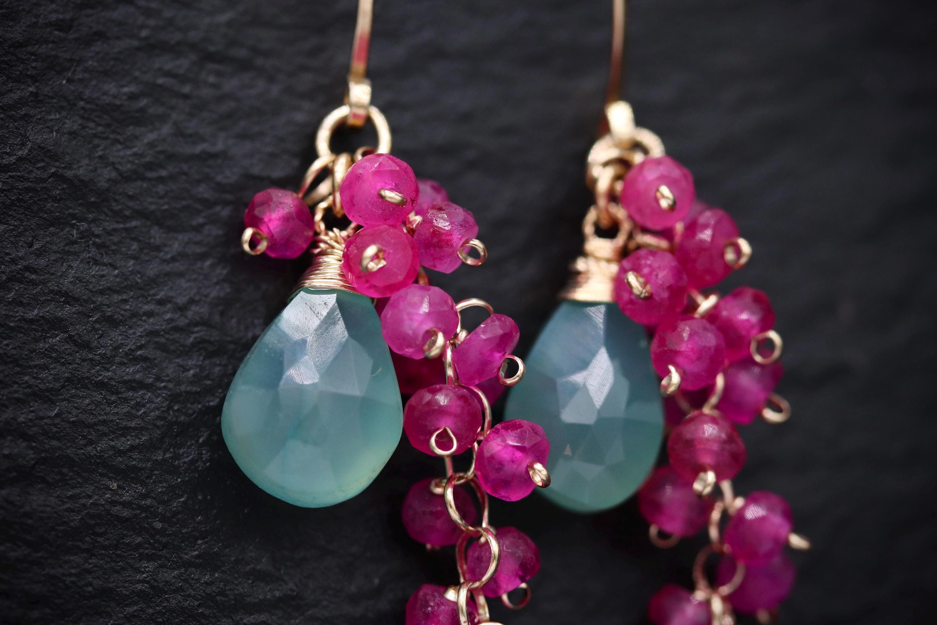 A pair of earrings with teal-colored stones and pink gemstones hanging from the ear hooks.