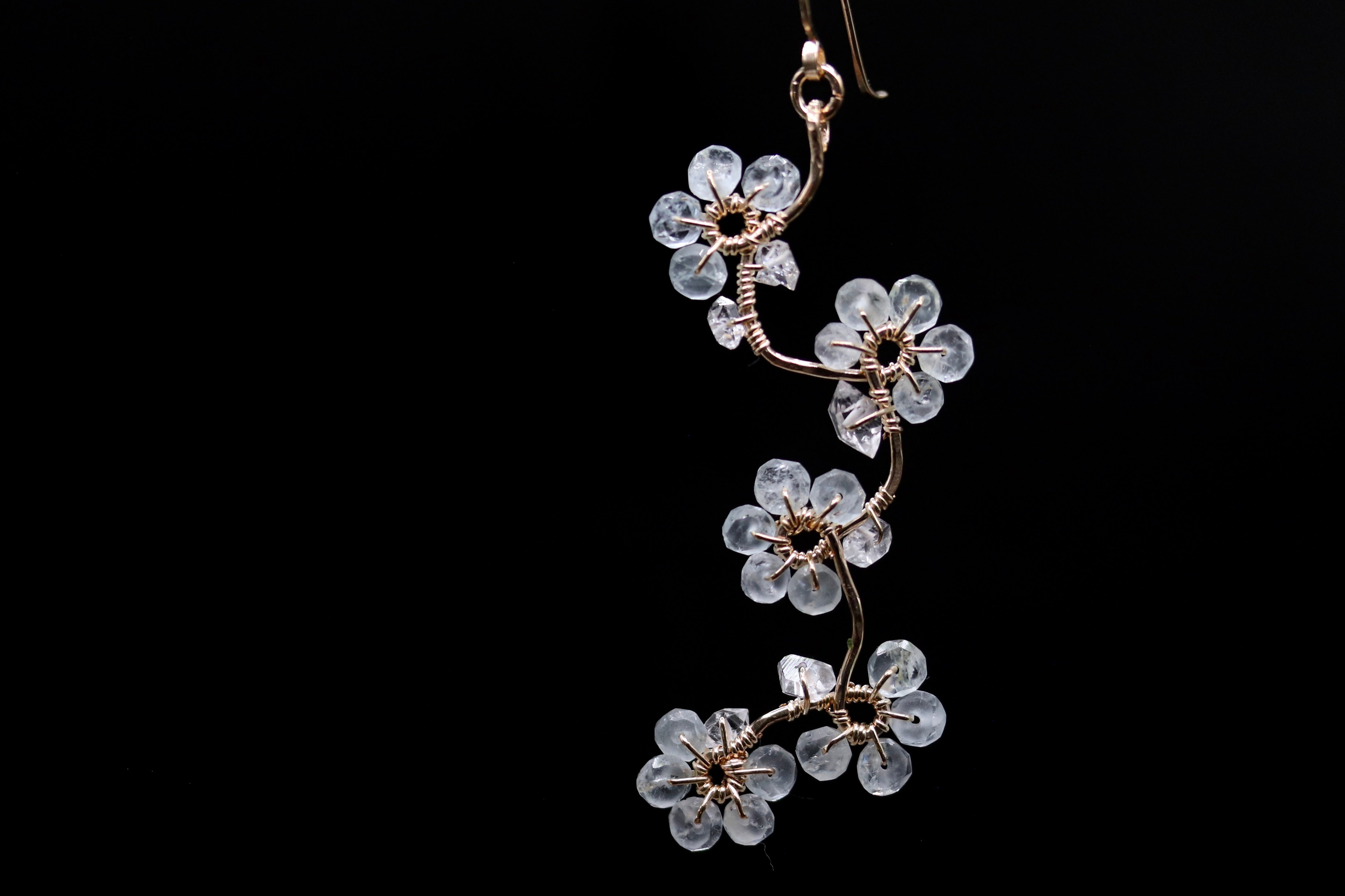 A delicate earring with a floral design made of clear crystal or glass, suspended against a black background.