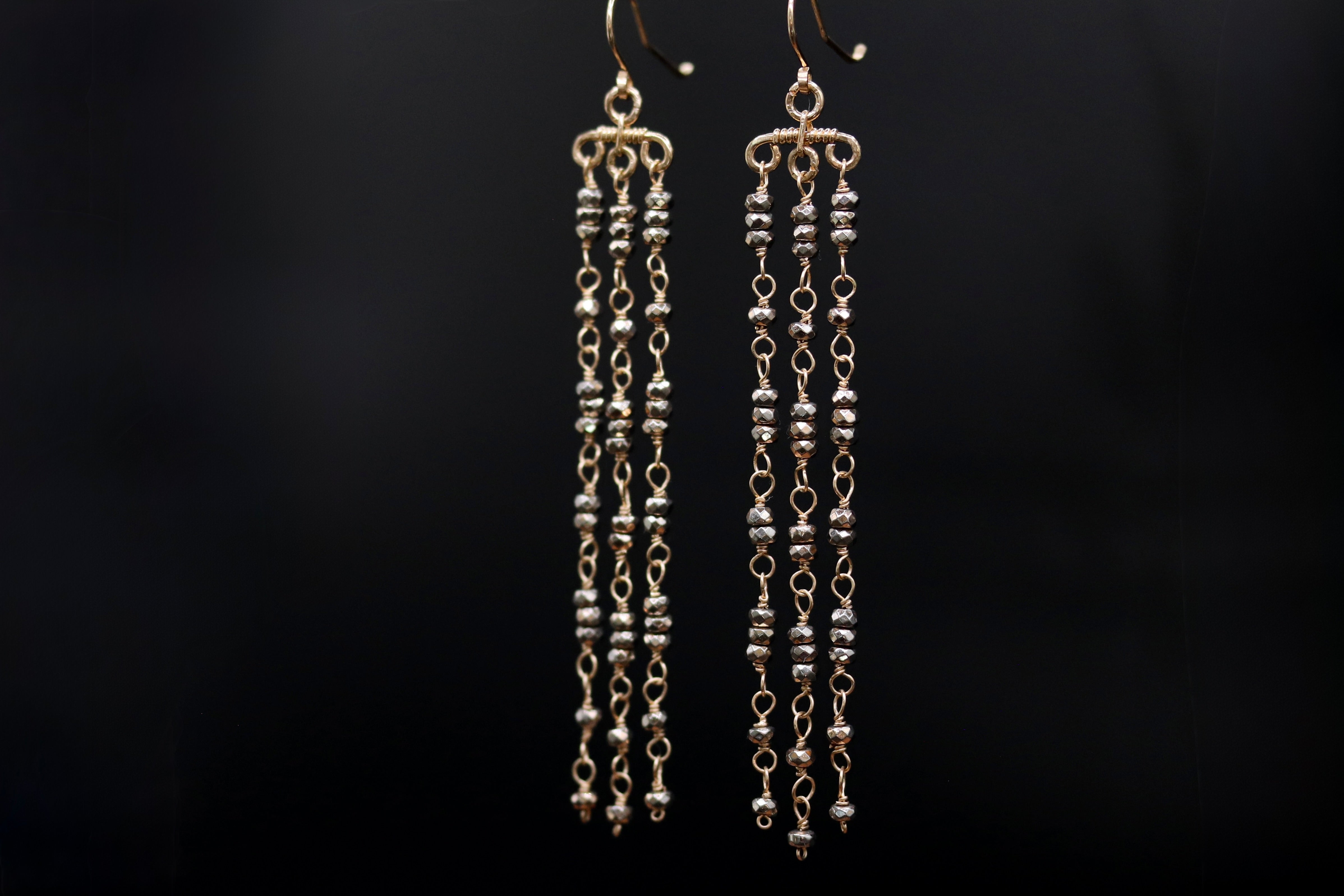 A pair of gold-colored earrings with long, dangling chains and small beads hanging from them.