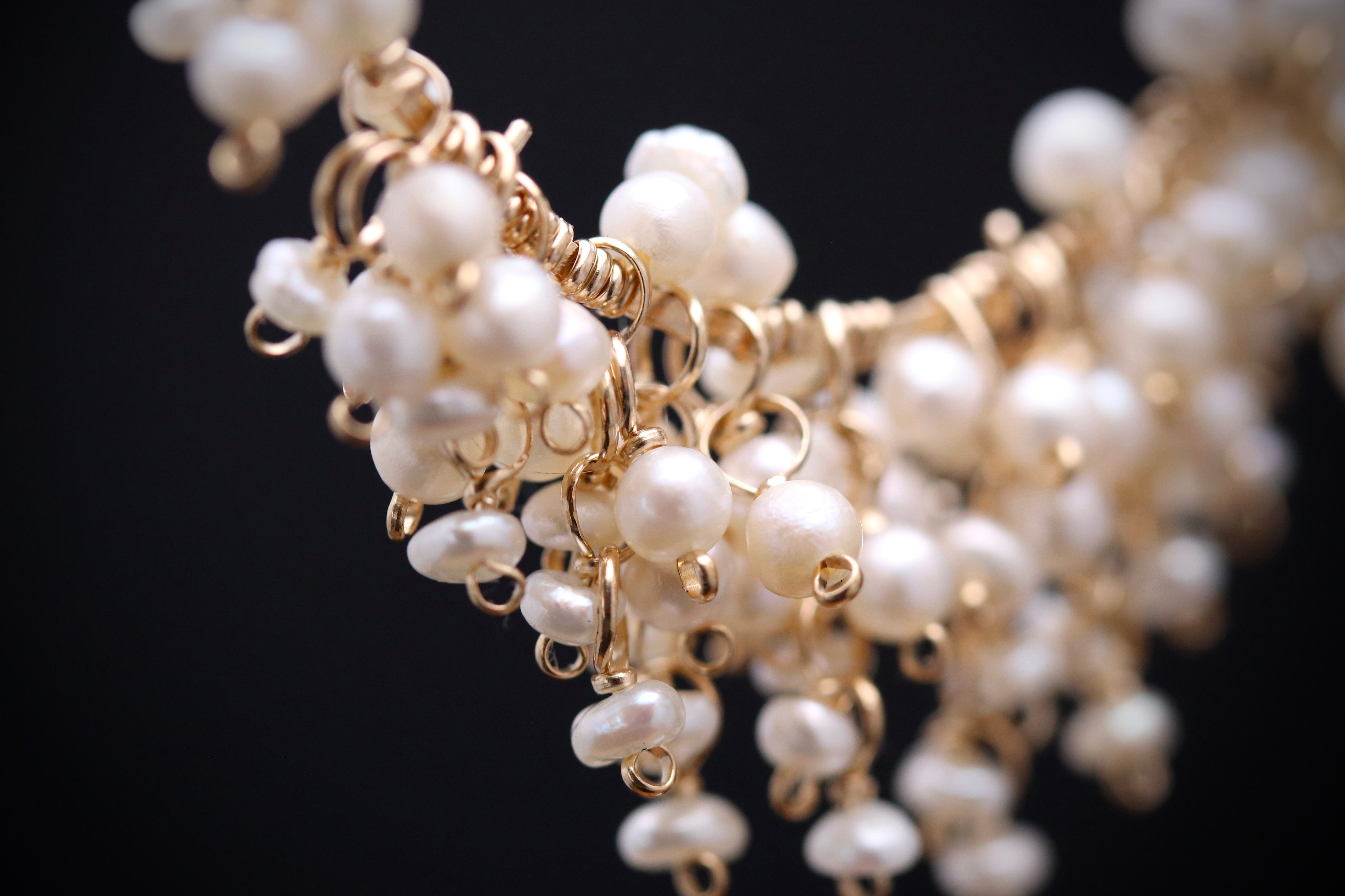 A close-up view of a delicate gold chain necklace adorned with numerous small, white pearls.