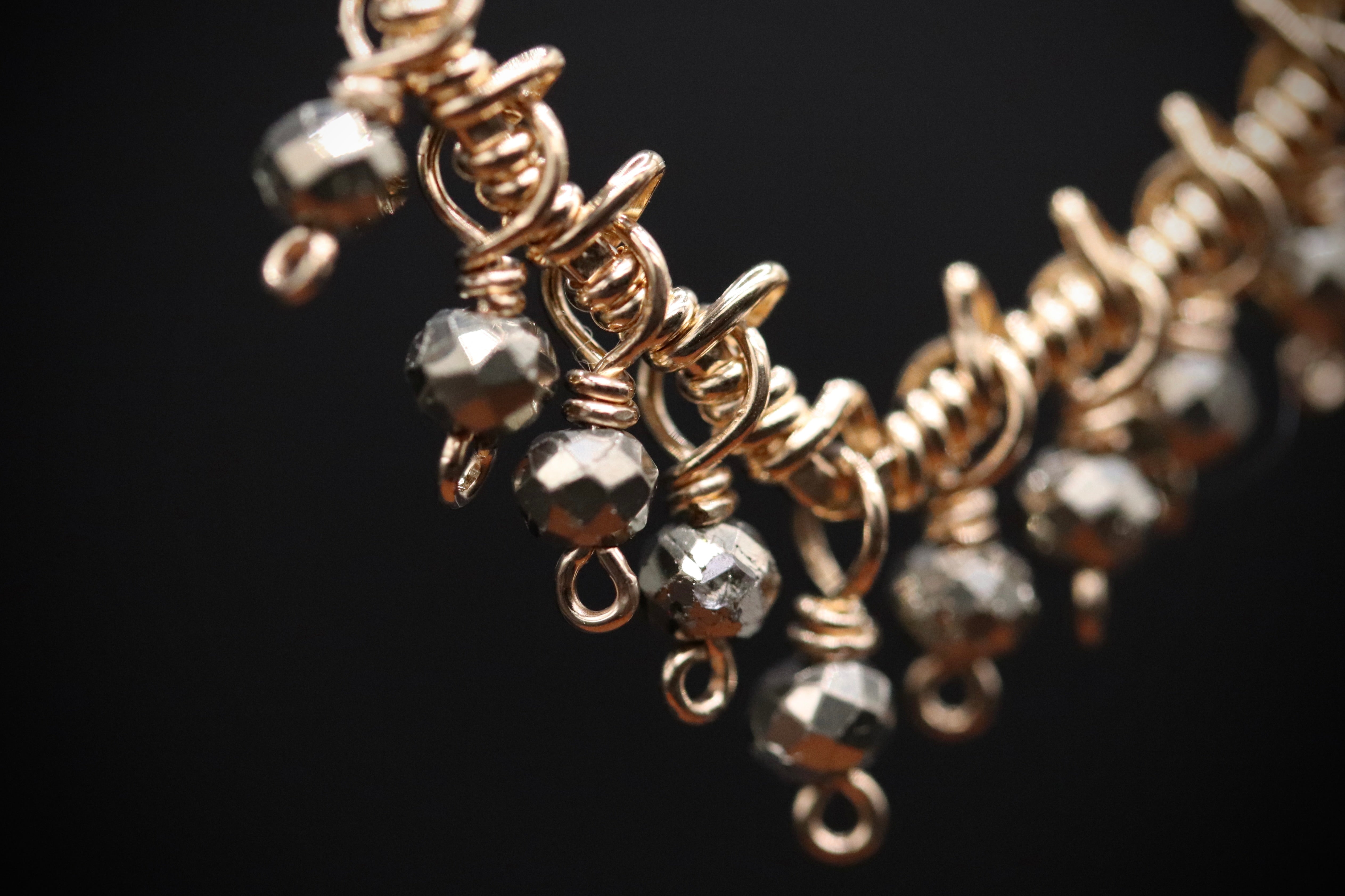 A close-up view of a gold-colored necklace with numerous small, round beads or stones attached to it, creating a decorative and intricate design.