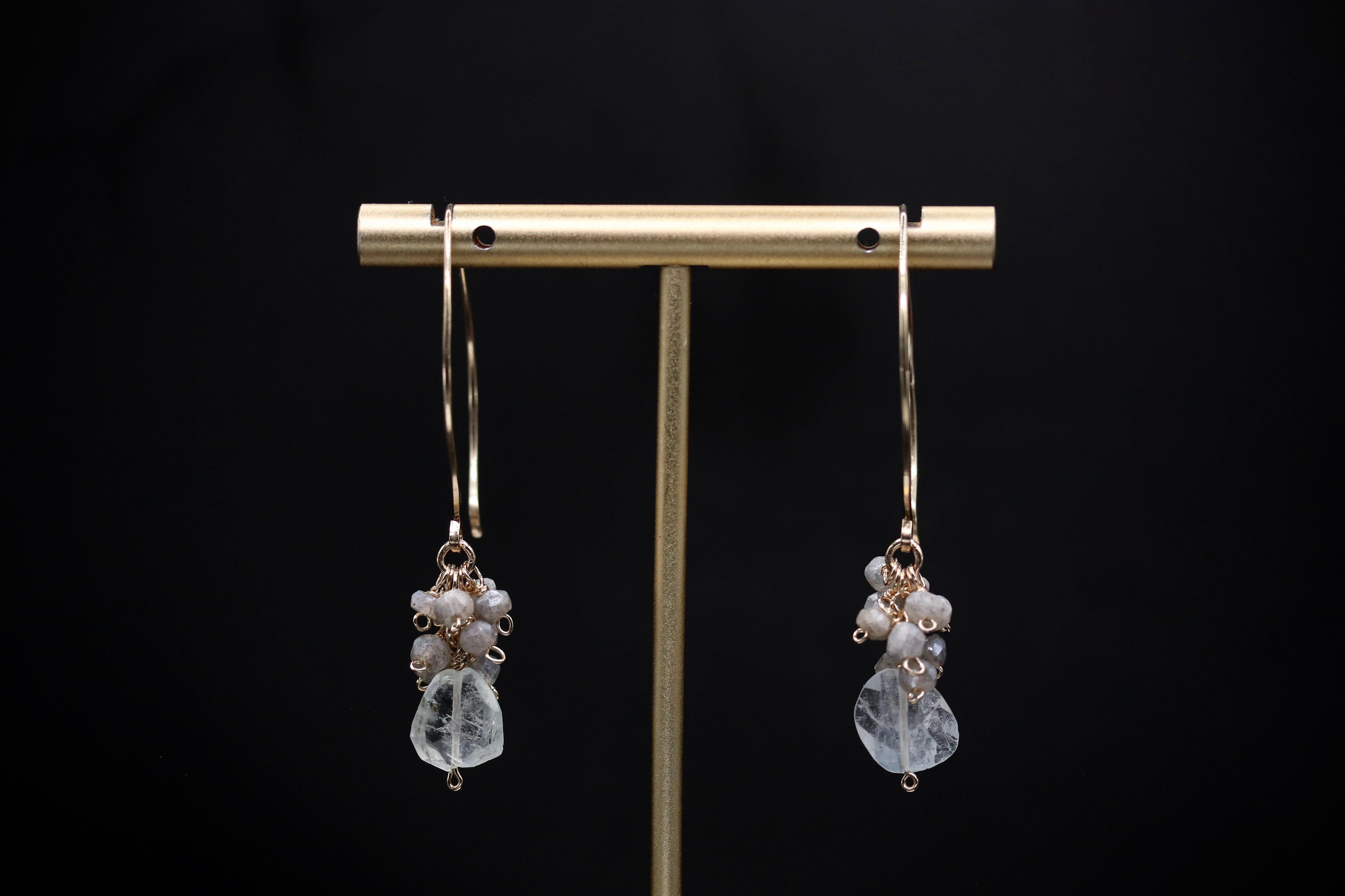 A pair of elegant earrings with clear gemstone accents, displayed on a gold stand against a black background.
