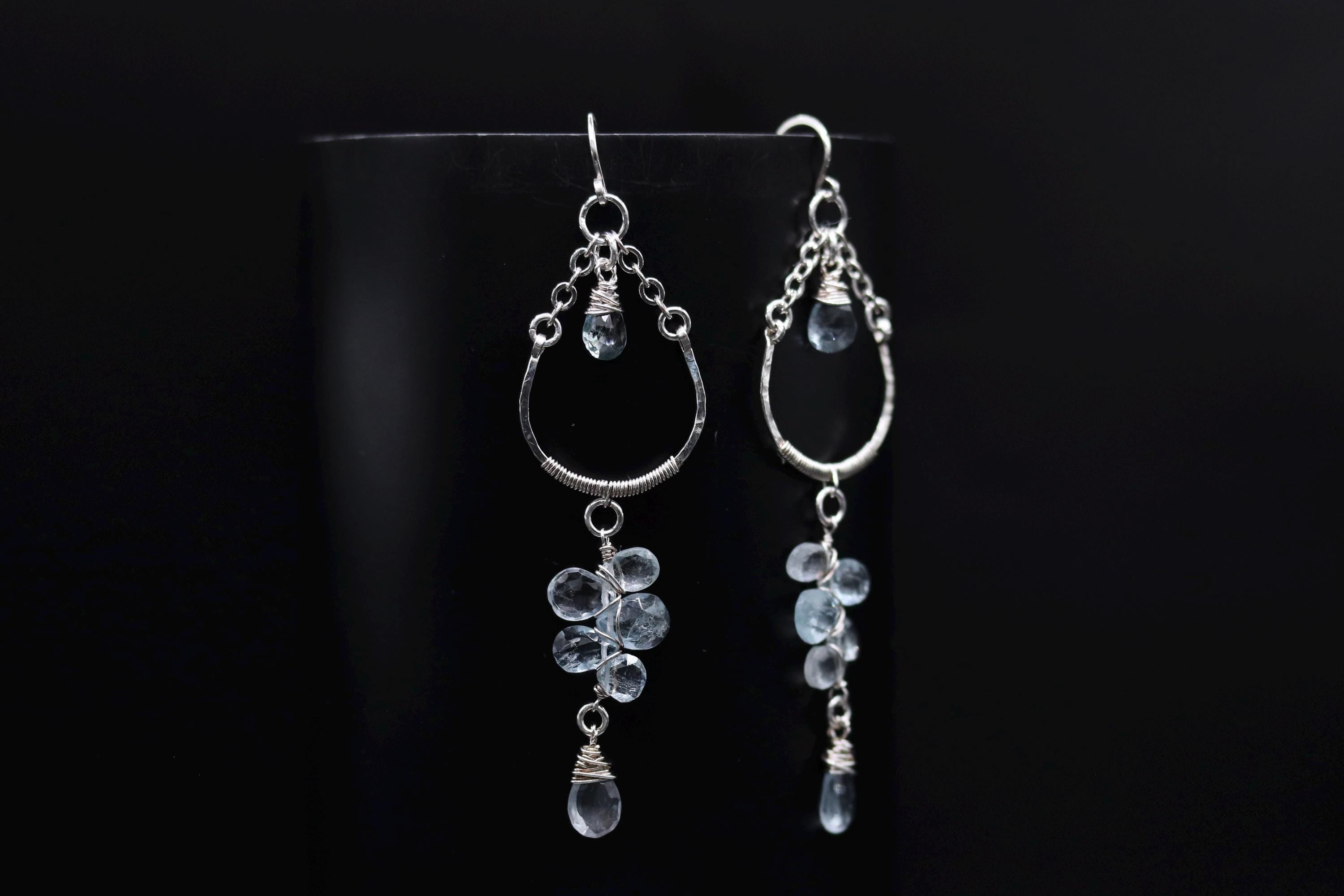 A pair of elegant silver earrings with dangling crystal stones against a black background.