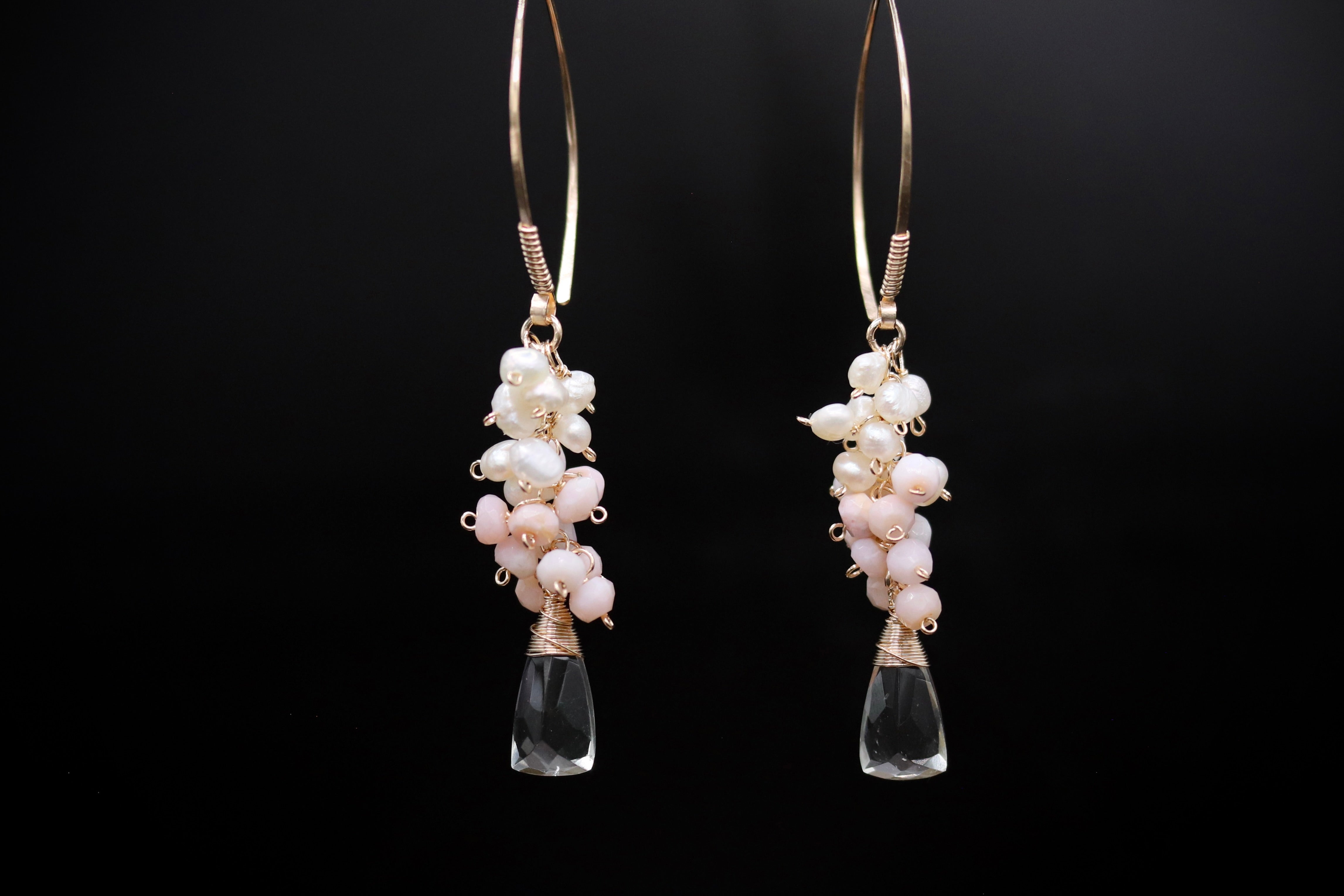 A pair of elegant earrings with clear glass pendants and white pearl accents, suspended from gold hooks against a black background.