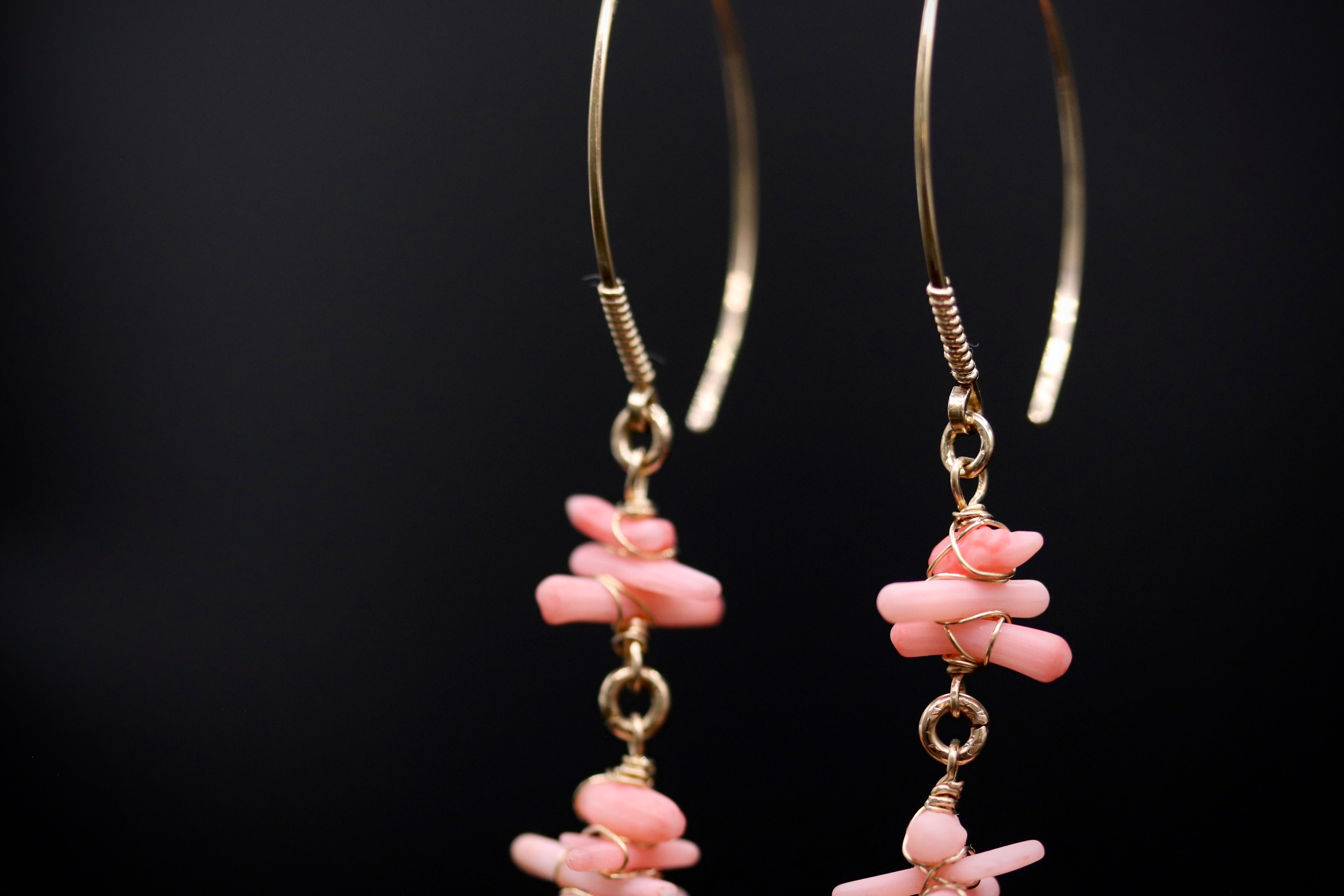 A pair of gold earrings with pink coral beads hanging from them against a black background.