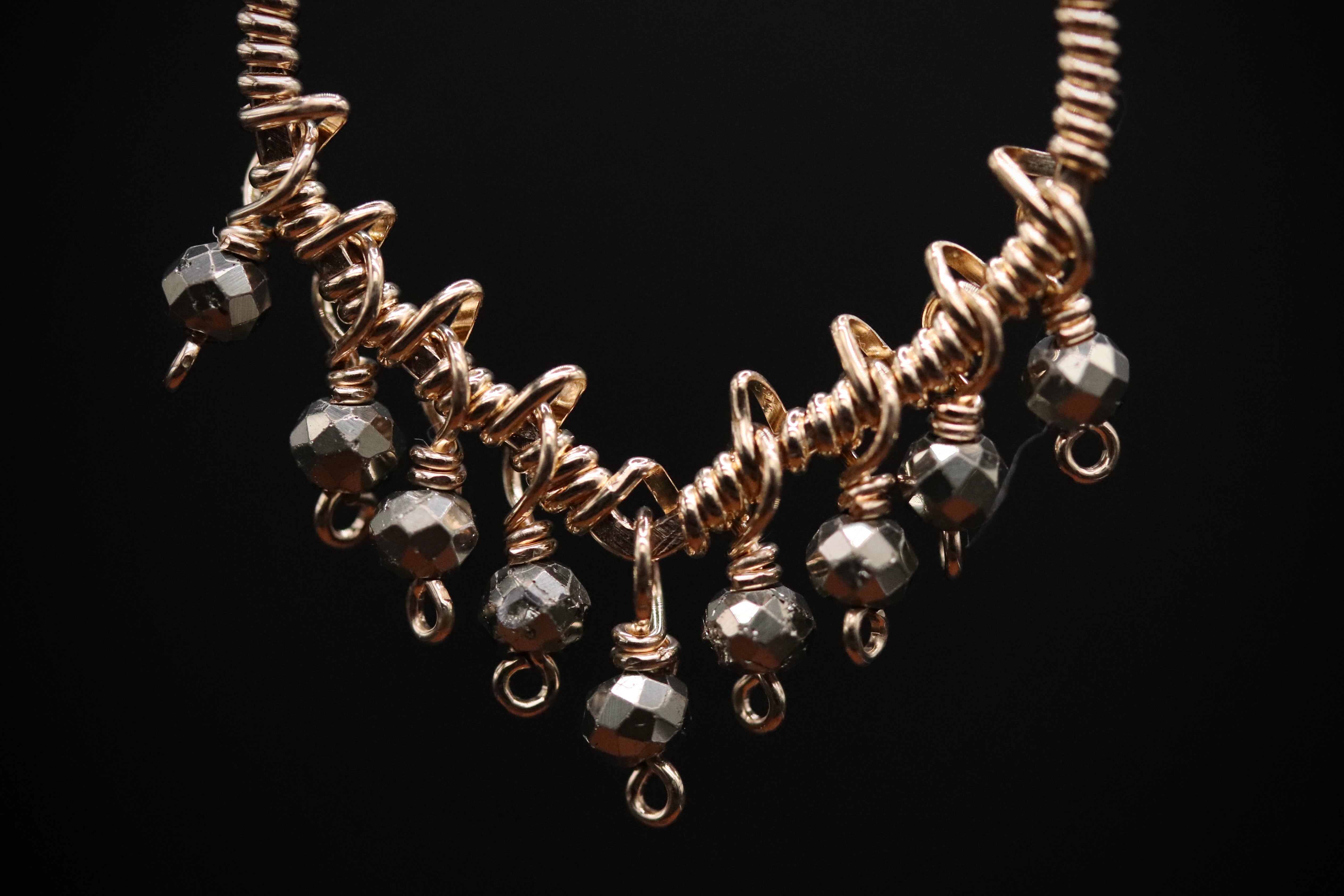 A close-up view of a gold-colored necklace with a twisted metal design and small metal beads hanging from it.
