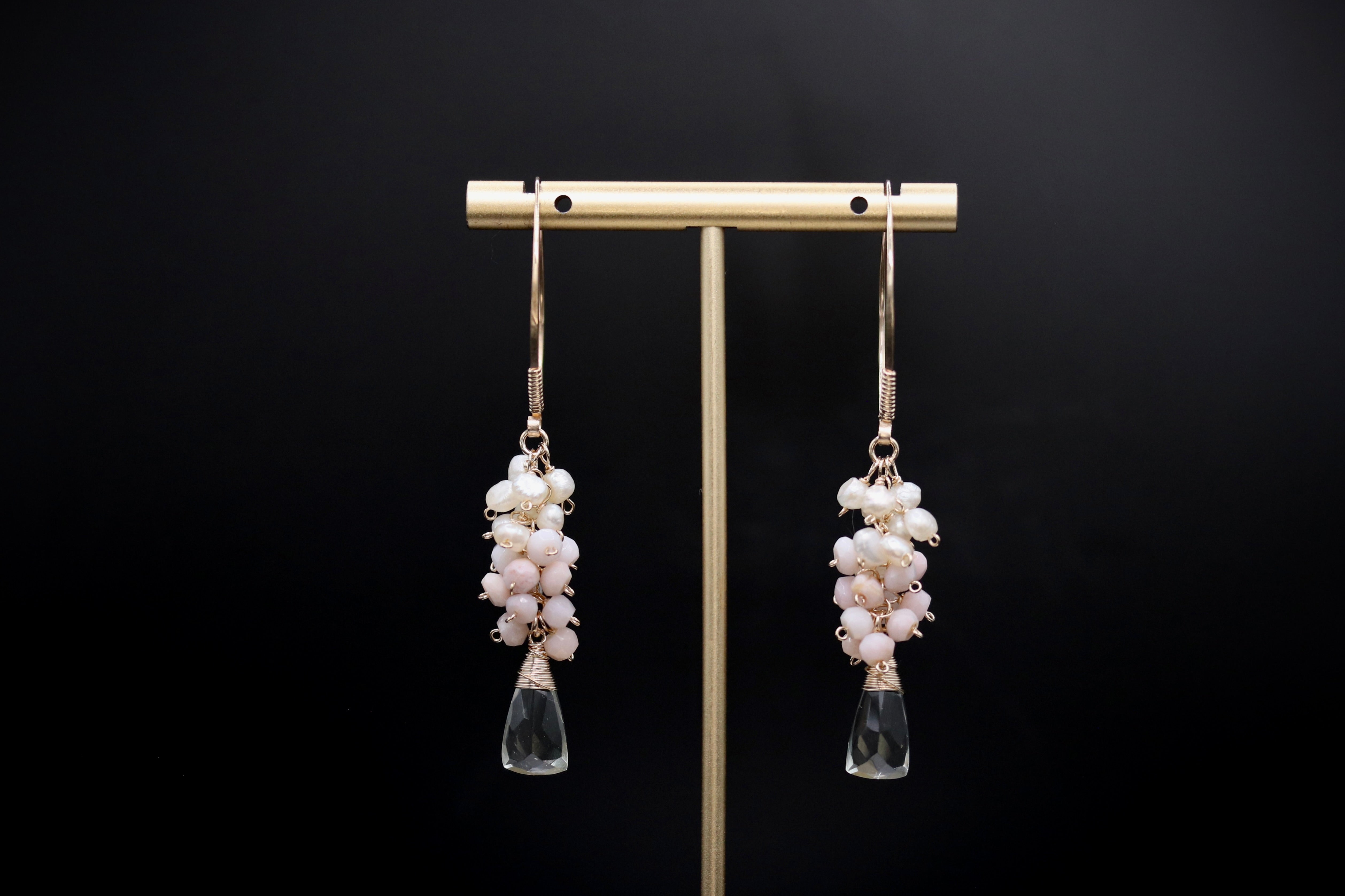 A pair of elegant earrings with clear gemstone accents and dangling crystal elements, displayed on a gold stand against a black background.
