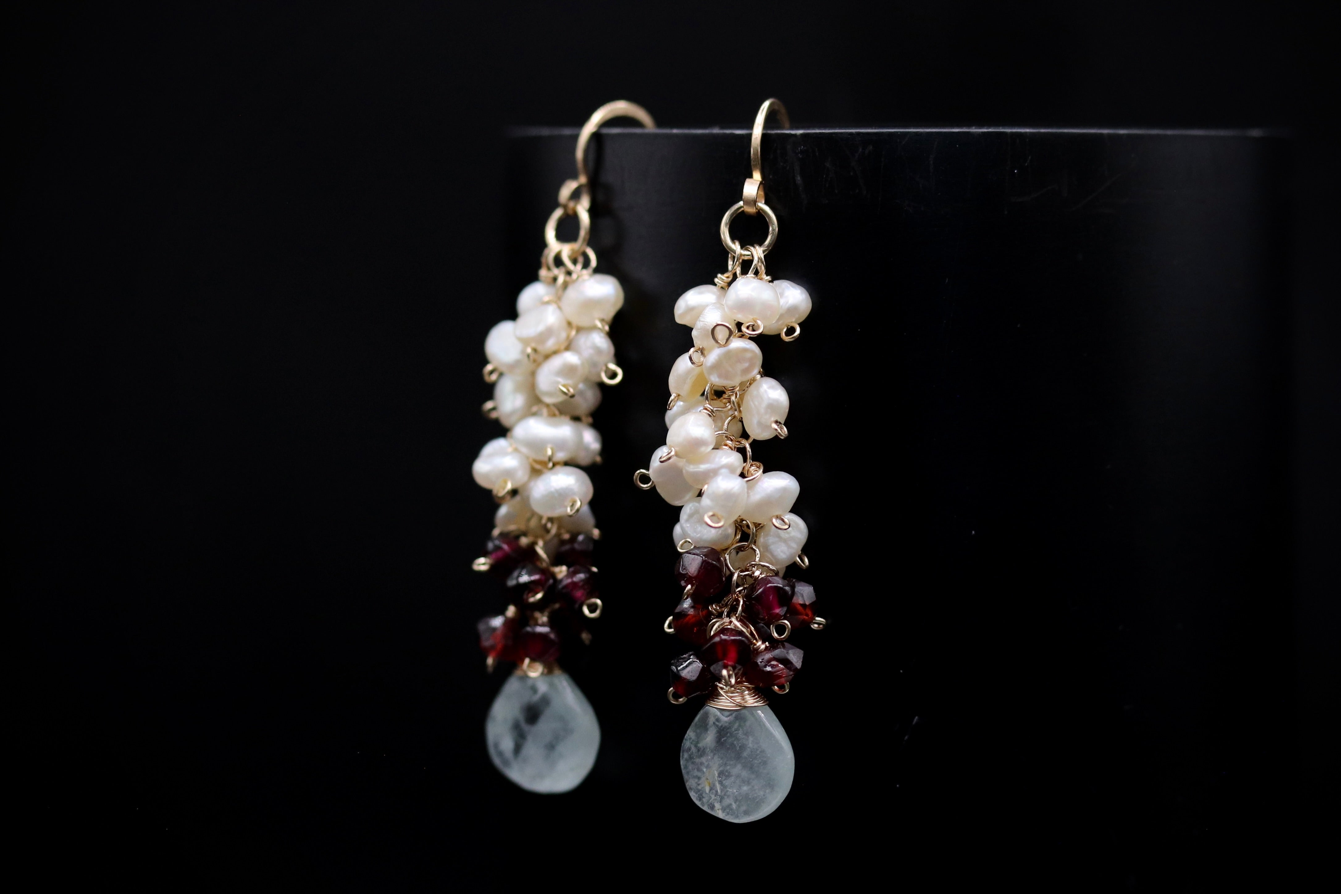 A pair of elegant earrings with white and red beads, as well as white and red pearls, hanging from a hook against a black background.