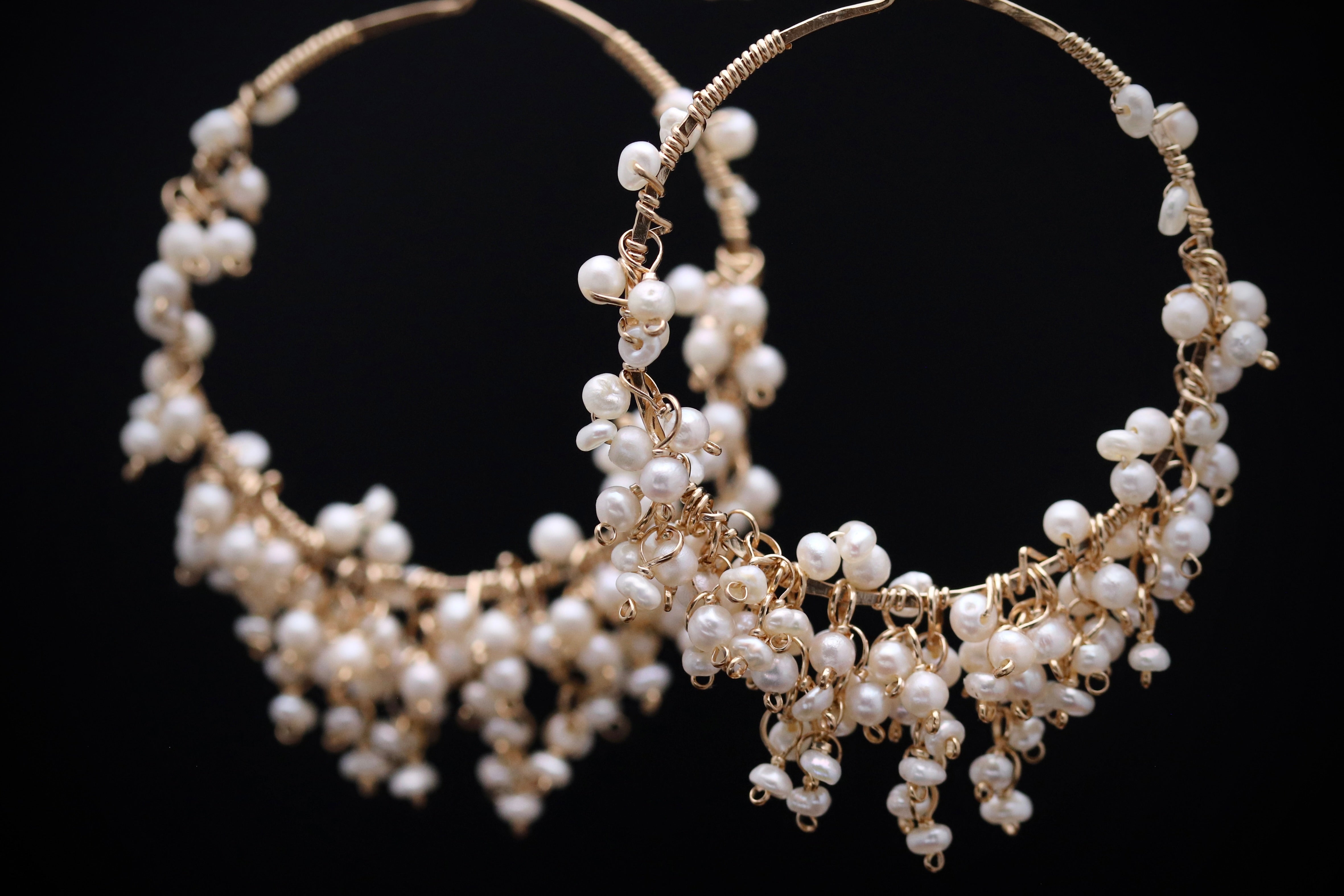 A pair of elegant earrings made of white pearls and gold wire, set against a black background.