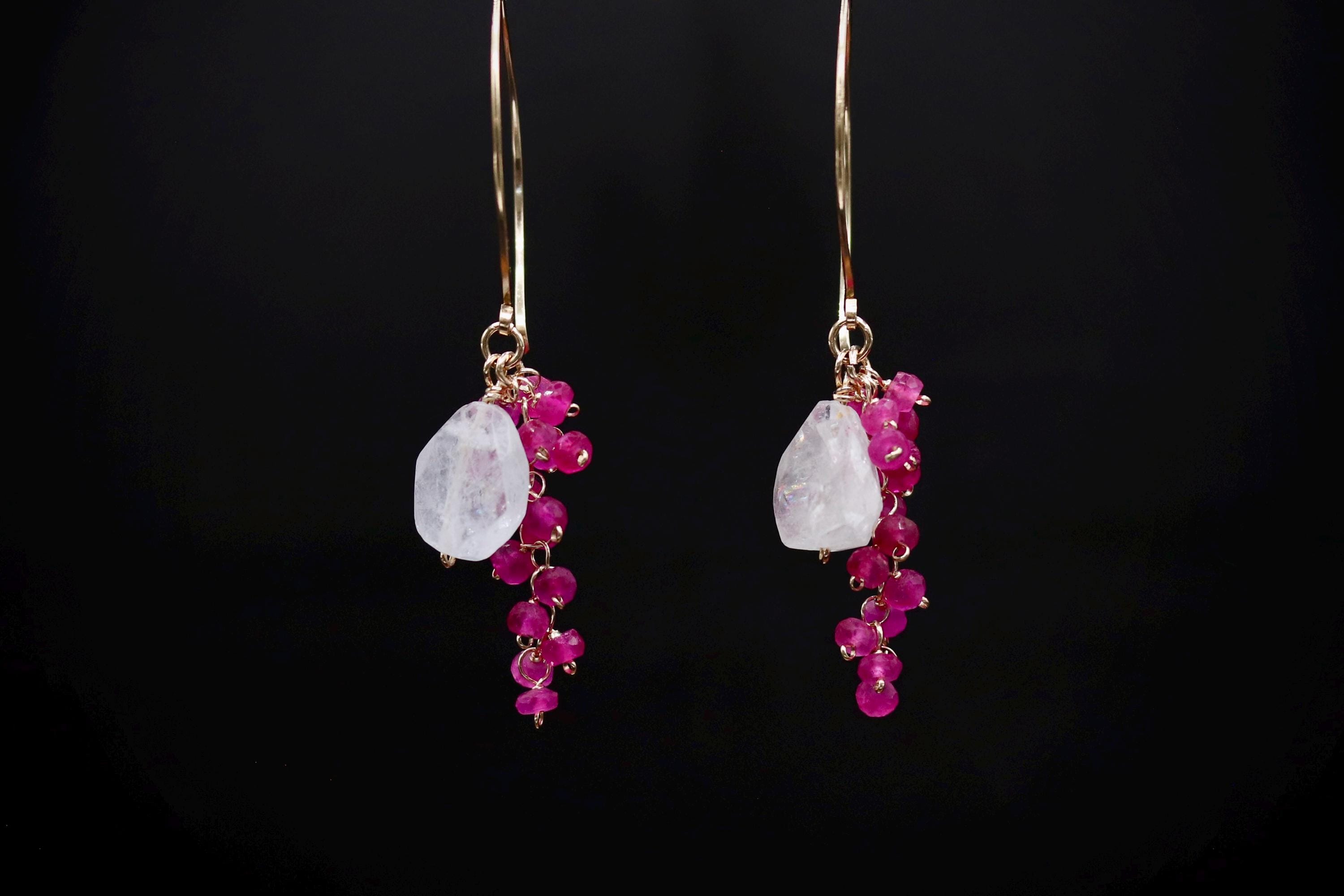 A pair of earrings with a combination of white and pink gemstones, as well as small, dangling beads in shades of pink.