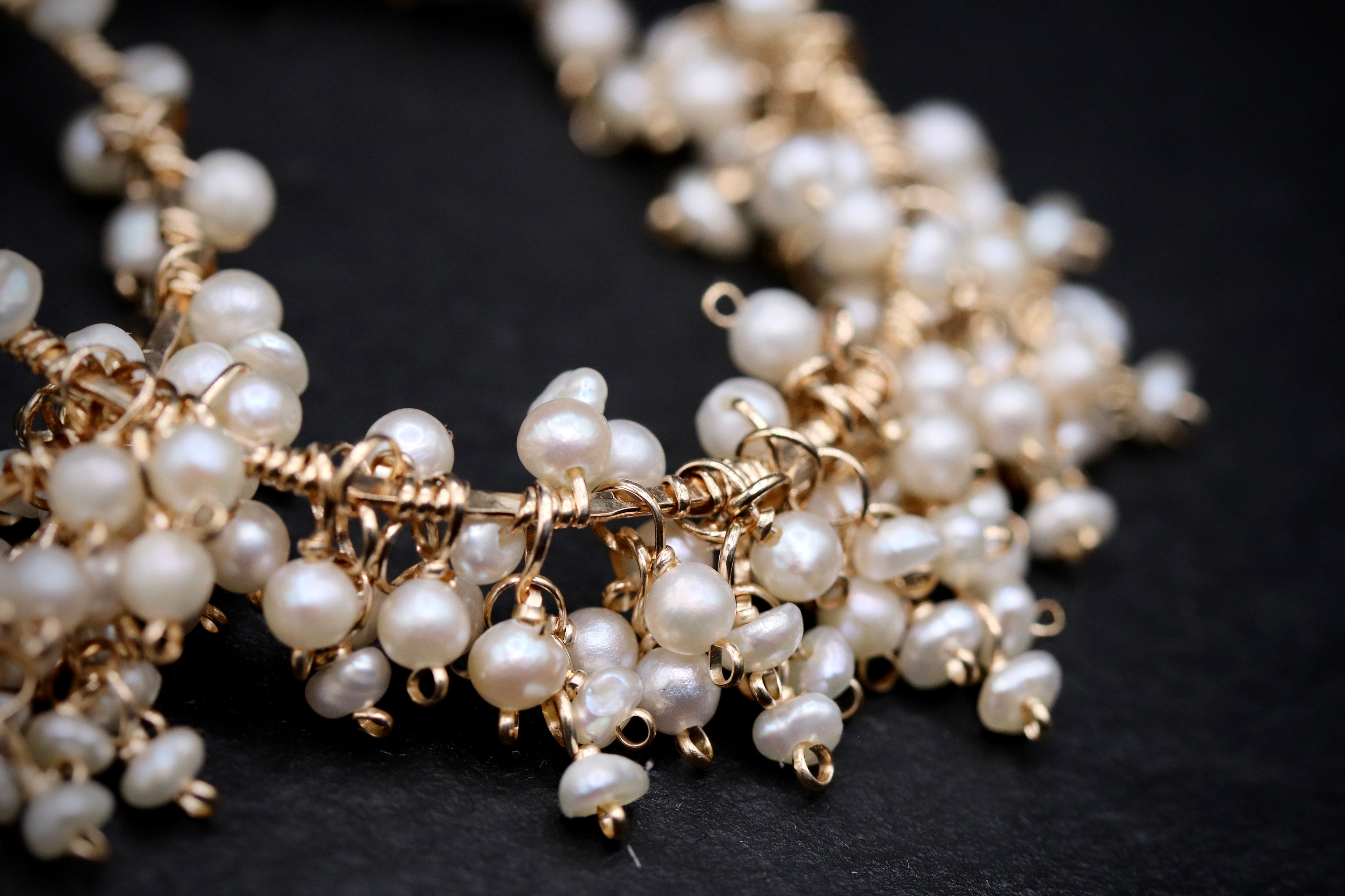 A close-up image of a delicate necklace with numerous small, white pearls and gold-colored metal charms.