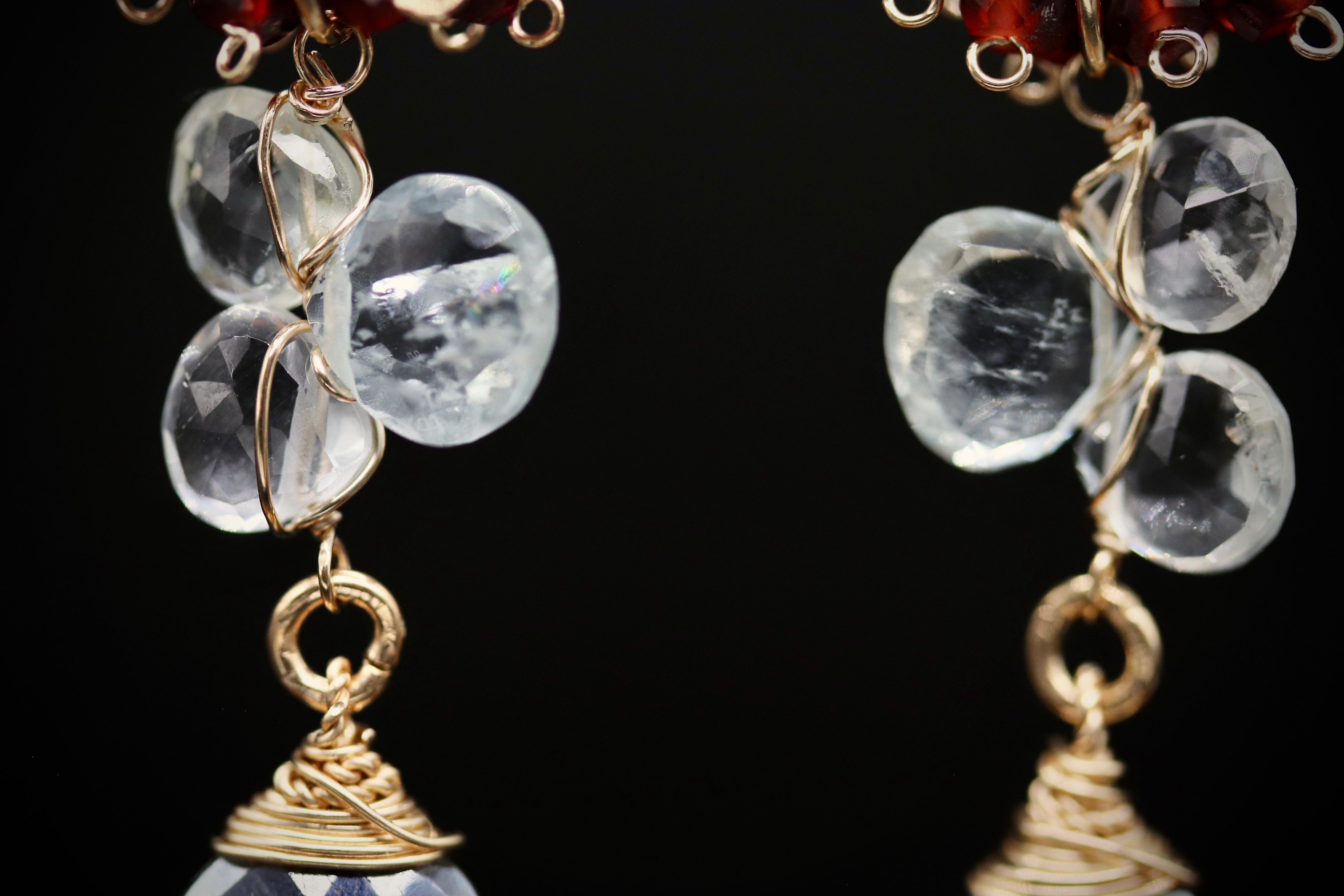 A close-up view of a pair of earrings with clear gemstones and metal wire accents, set against a black background.