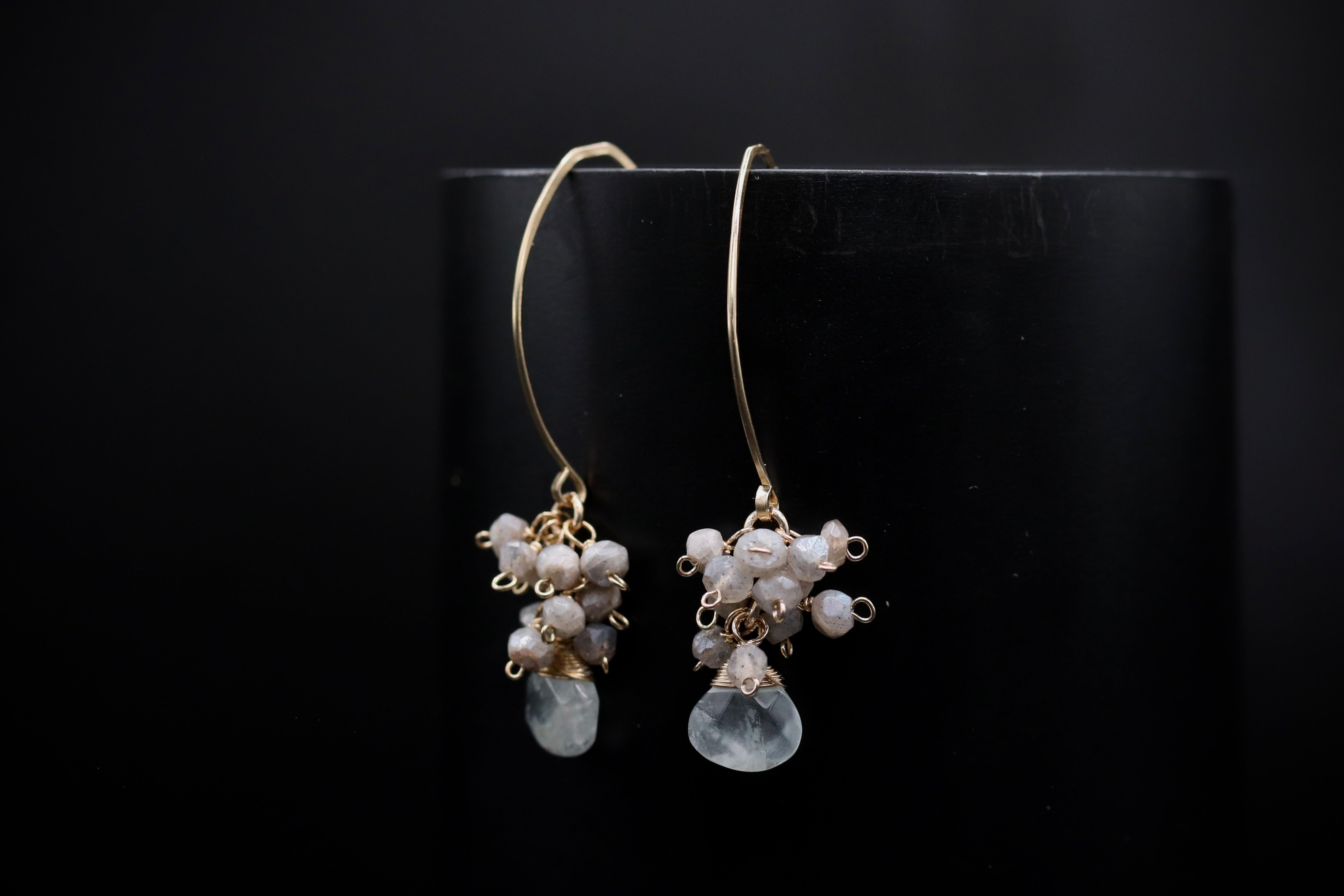 A pair of elegant earrings with white stones and gold accents, hanging from a black background.