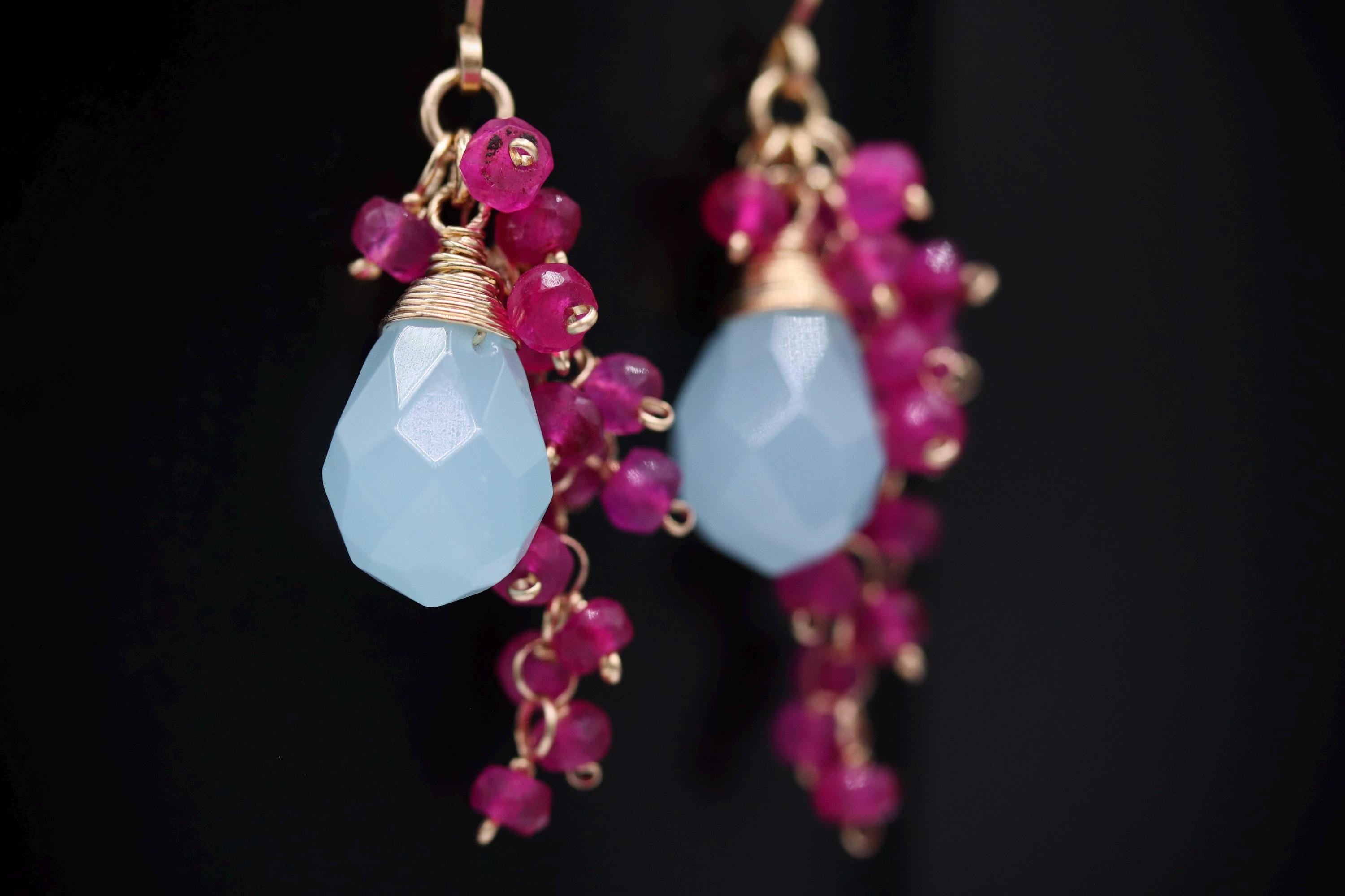 A pair of earrings with a blue stone and pink beads hanging from the ear hooks.