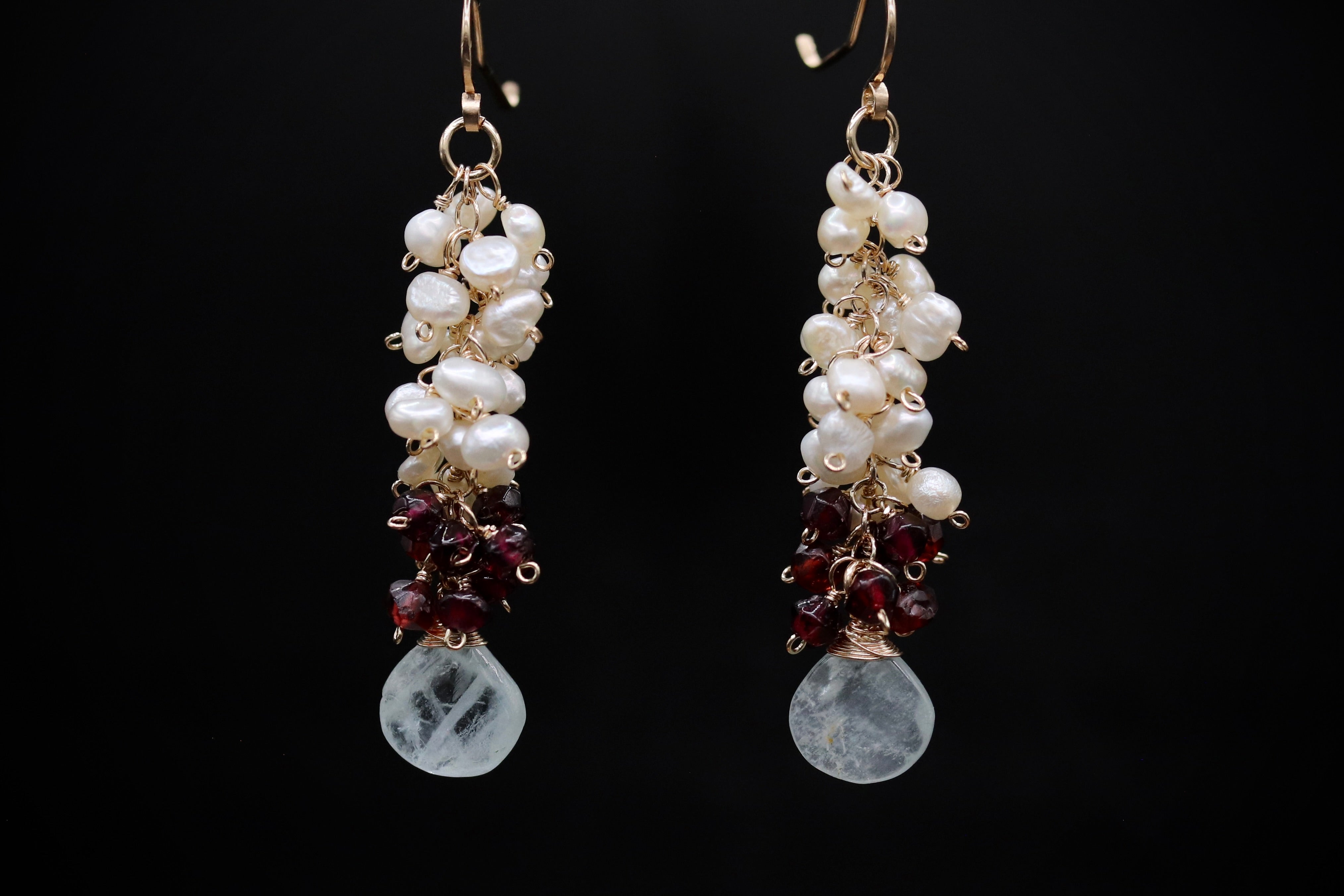 A pair of elegant earrings with white pearls, garnet stones, and a clear crystal pendant.